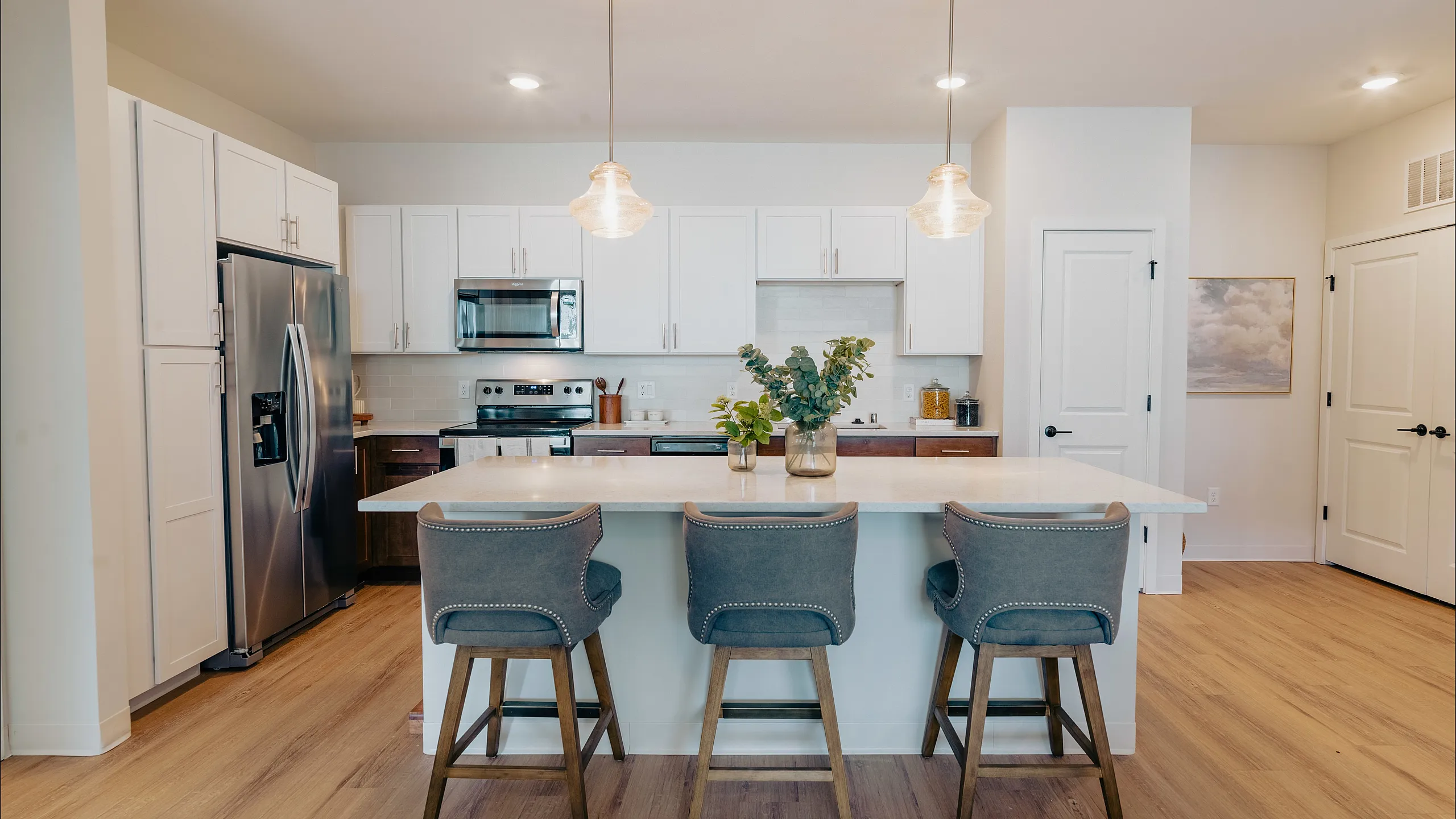 Modern kitchen with stylish pendant lighting, white cabinetry, stainless steel appliances, and a chic island with plush bar stools.