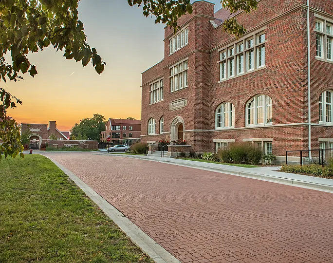 Charming brick building with classic architectural details, surrounded by lush greenery and a serene evening setting.
