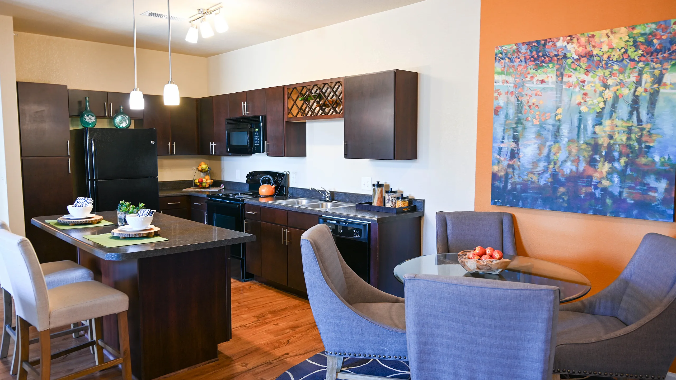 Modern kitchen with sleek dark cabinetry, stylish island seating, and a cozy dining nook adorned with vibrant wall art.