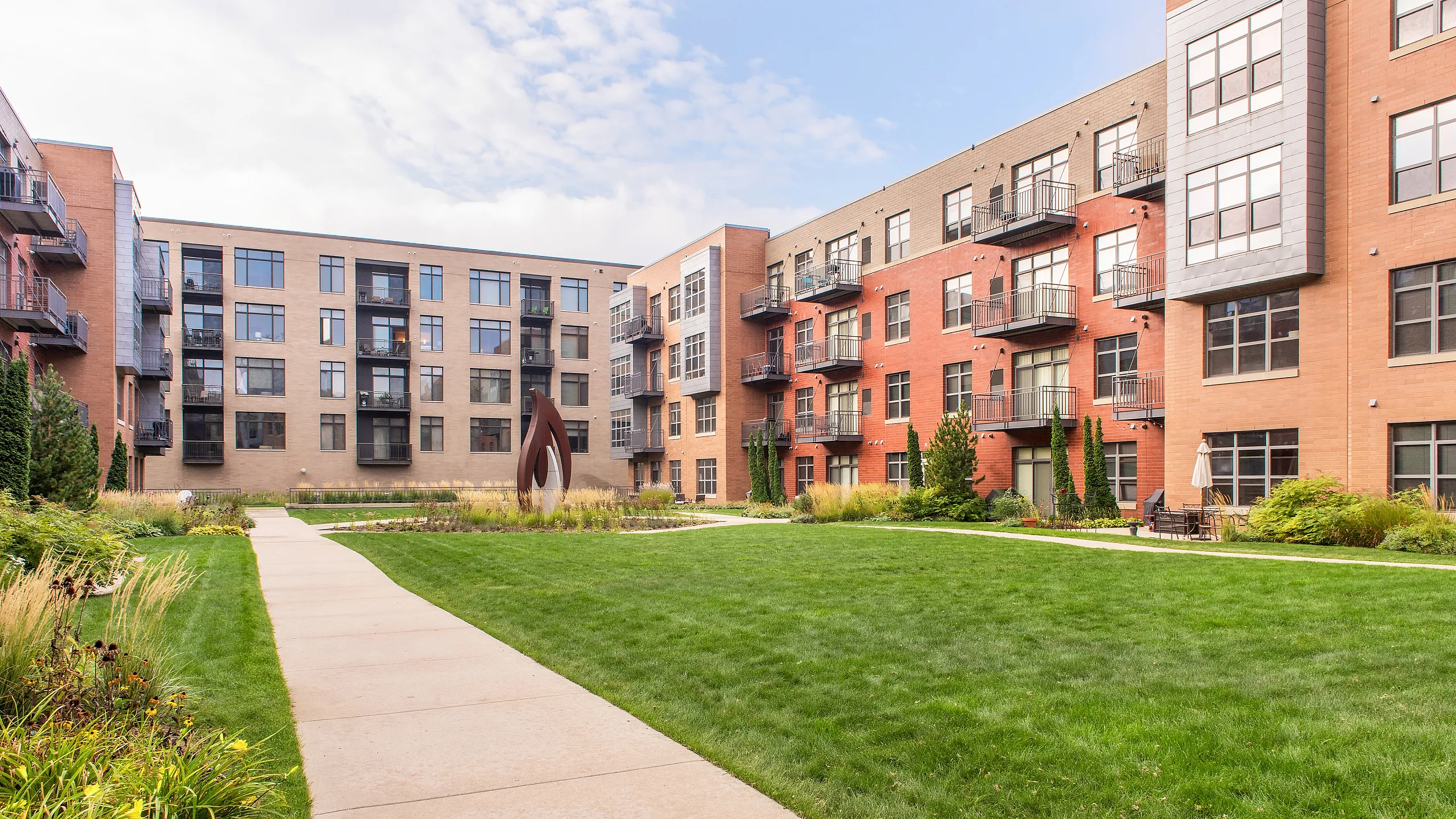 Charming apartment complex with modern brick facade, lush green courtyard, and inviting pathways, perfect for urban living.