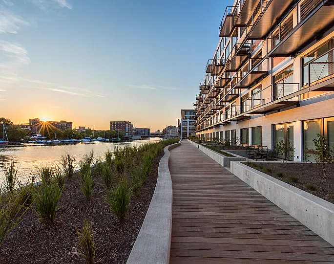 Modern riverside apartments with expansive balconies overlooking a serene waterfront at sunset.