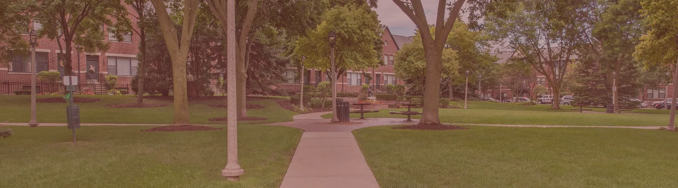 Charming walkway through lush green park with elegant street lamps and vibrant trees, leading to cozy apartments.