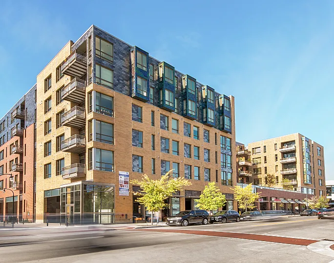 Modern apartment building with sleek design features, balconies, and large windows, set against a clear blue sky.