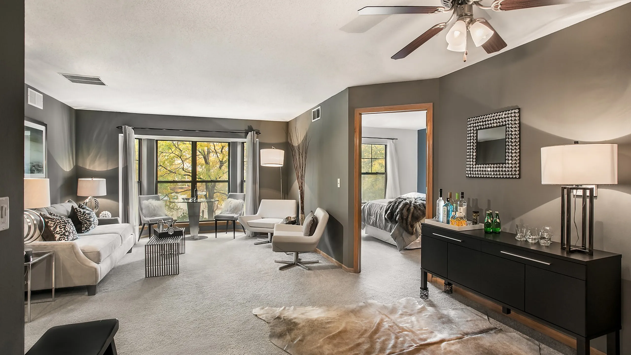 Elegant living room with modern decor, featuring a cozy seating area, large windows with a serene view, and a stylish bedroom entrance.