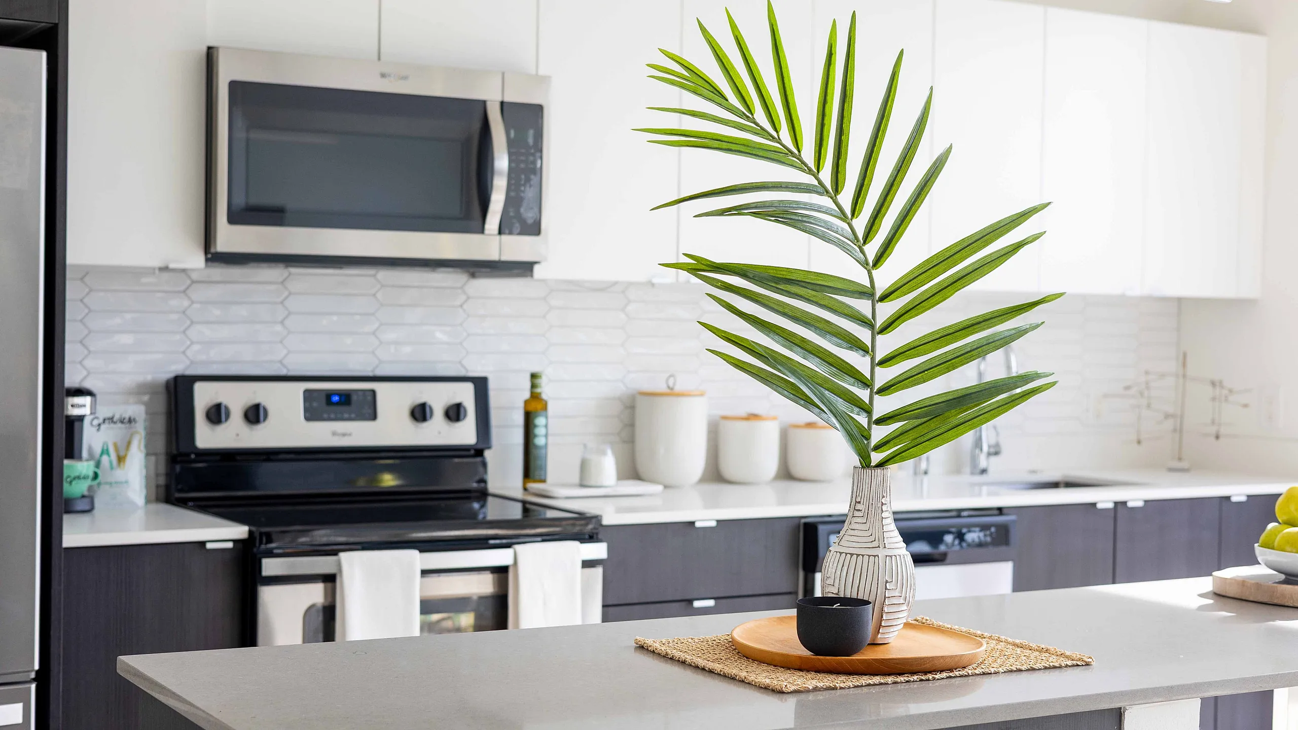 Modern kitchen with sleek stainless steel appliances, elegant white cabinetry, and a stylish island with decorative greenery.