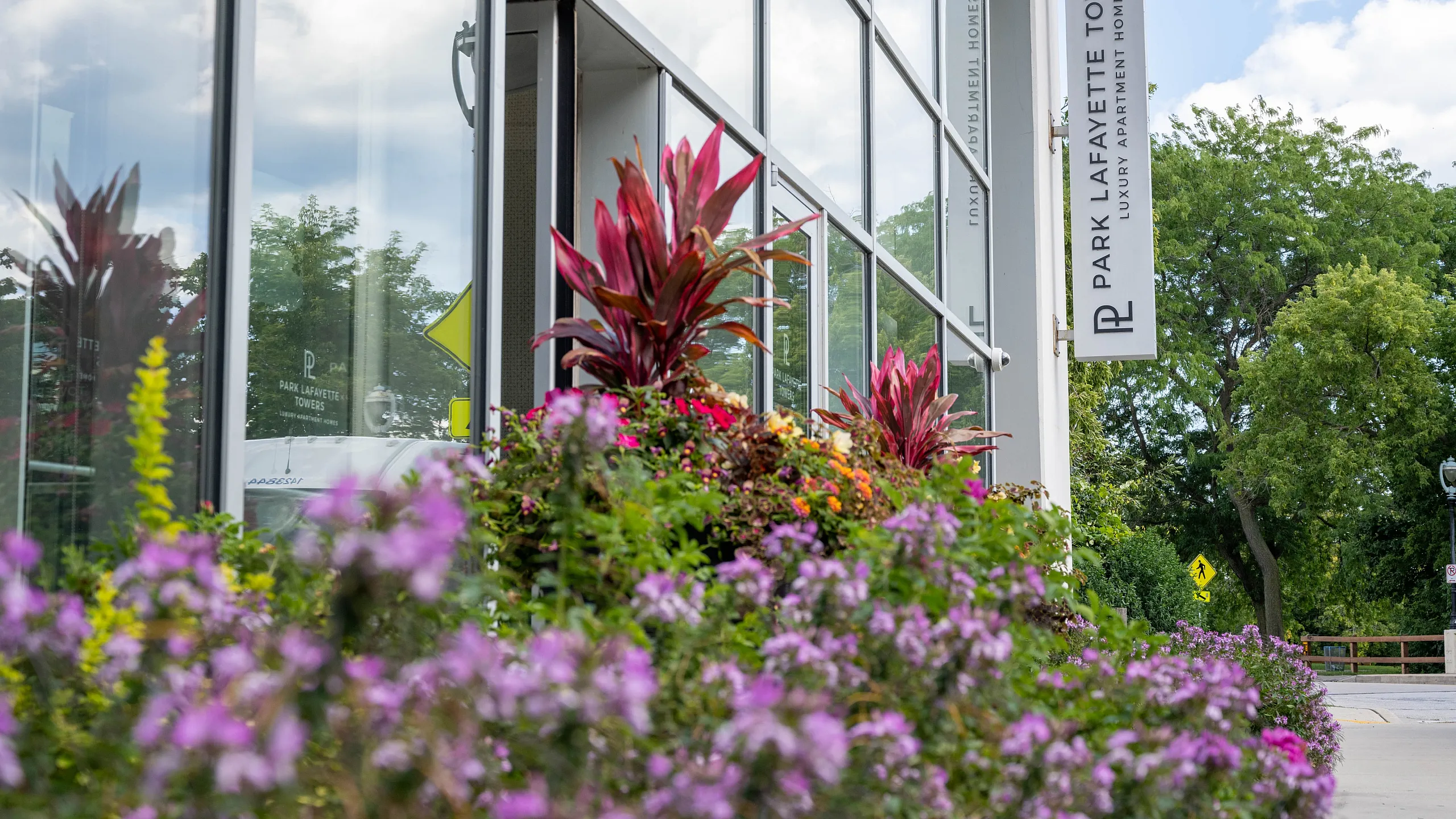 Bright and inviting entrance to Park Lafayette Towers with vibrant floral displays and sleek modern architecture.