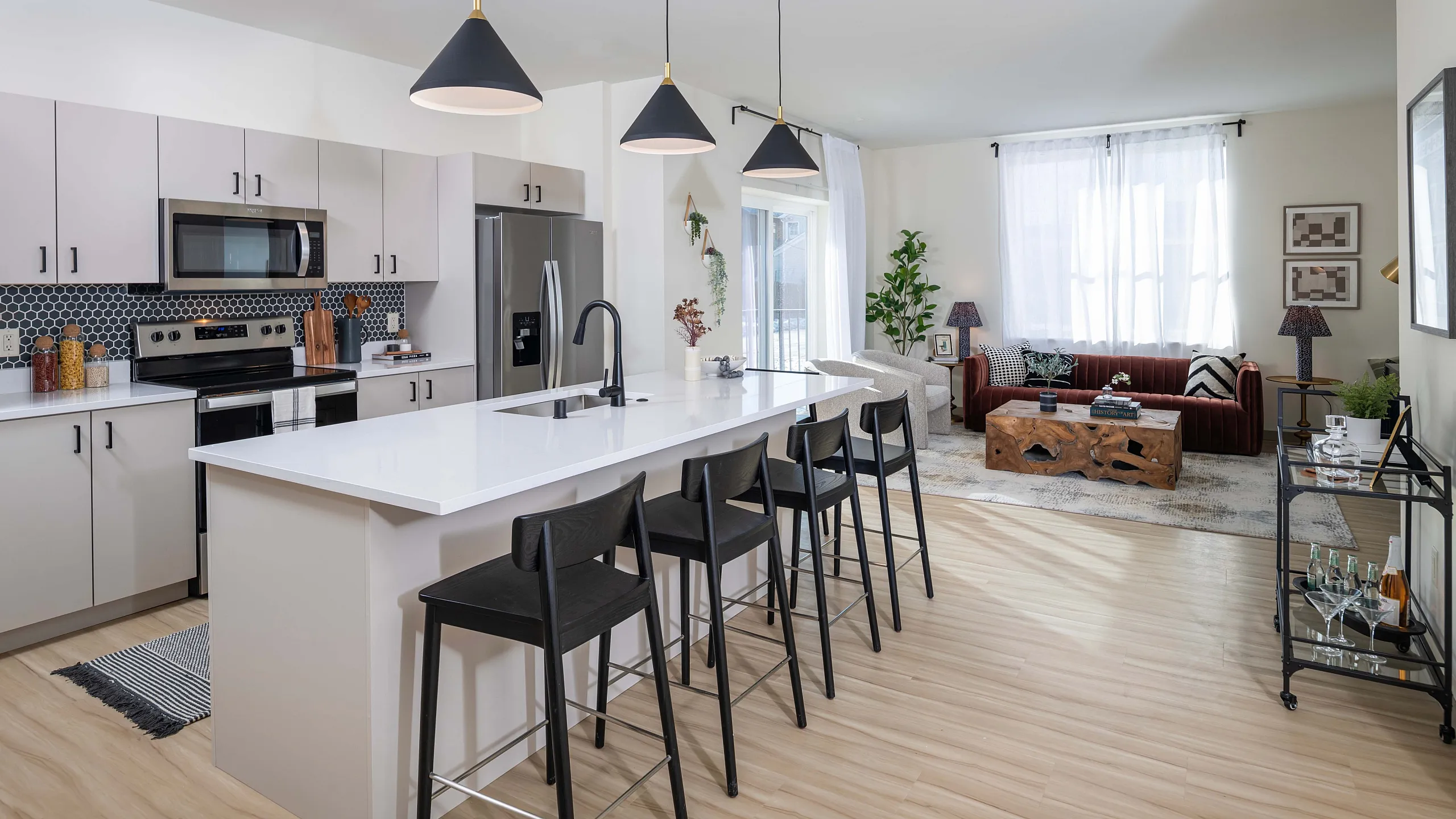 Modern open-concept kitchen with sleek white countertops and stylish pendant lighting, transitioning to a cozy living area with a plush sofa and natural light.