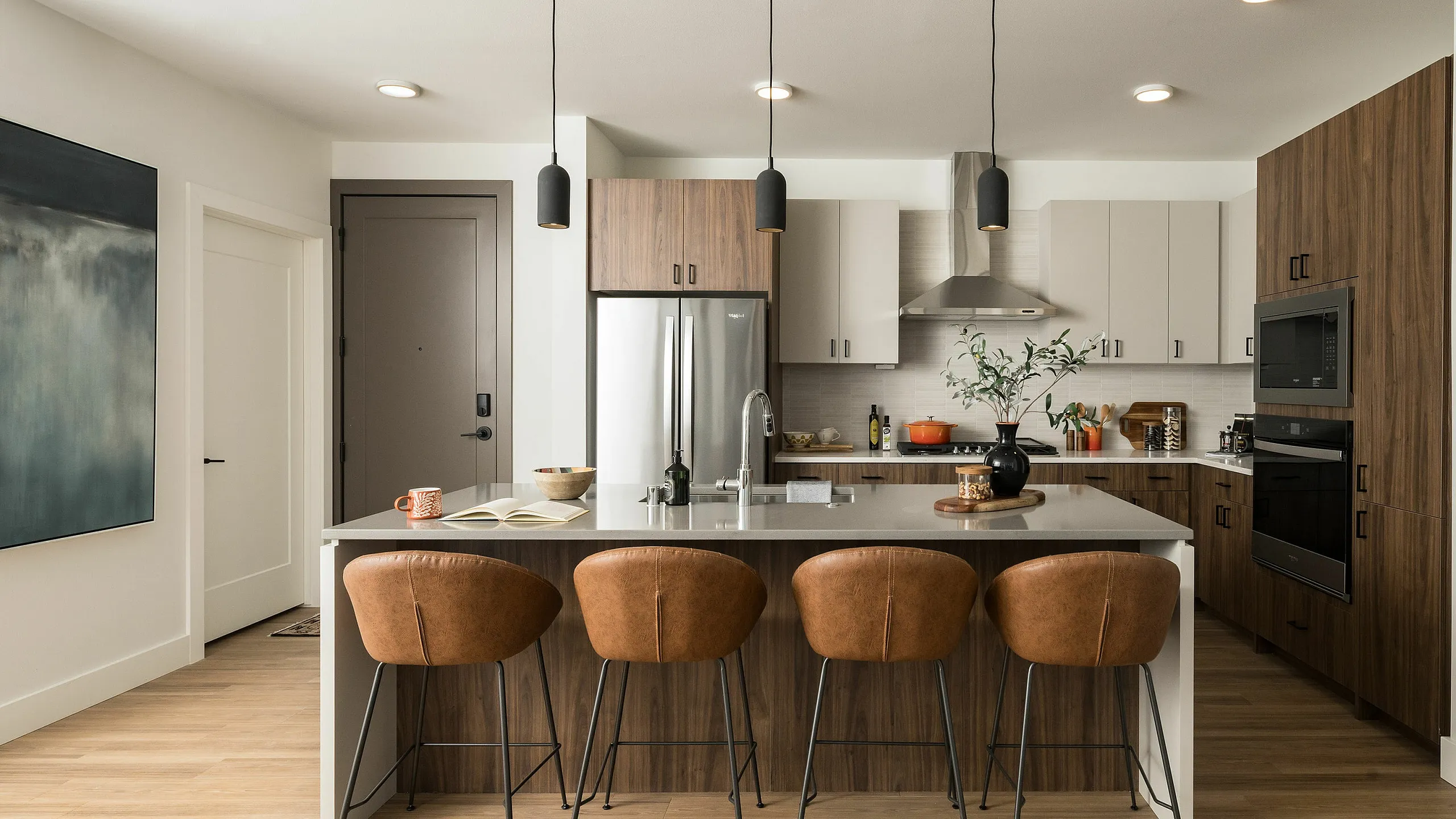Modern kitchen design featuring a sleek island with brown leather barstools, elegant pendant lighting, and stainless steel appliances.