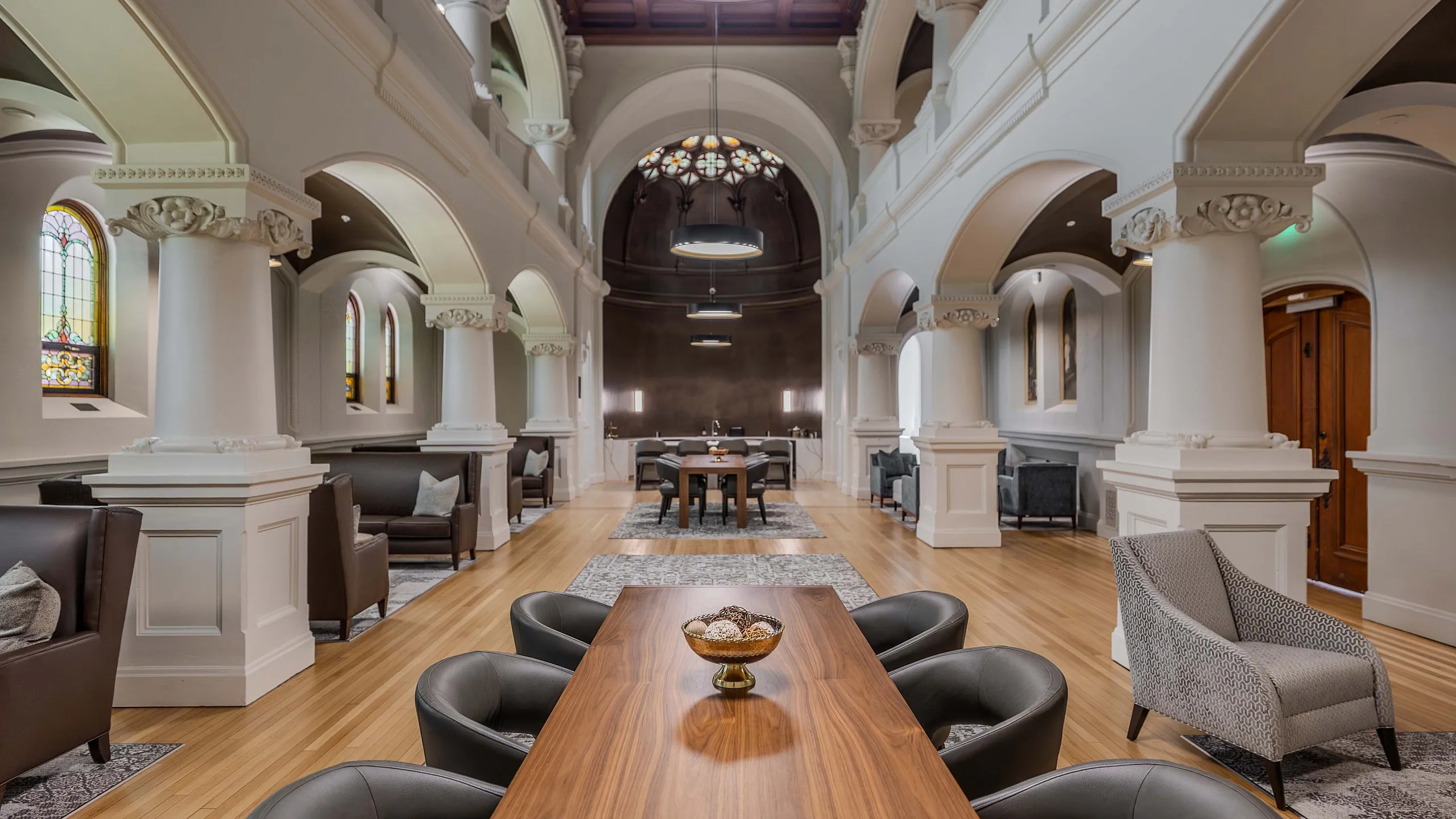 Elegant communal space with grand arches, luxurious seating, and a polished wooden table, exuding historic charm and modern sophistication.