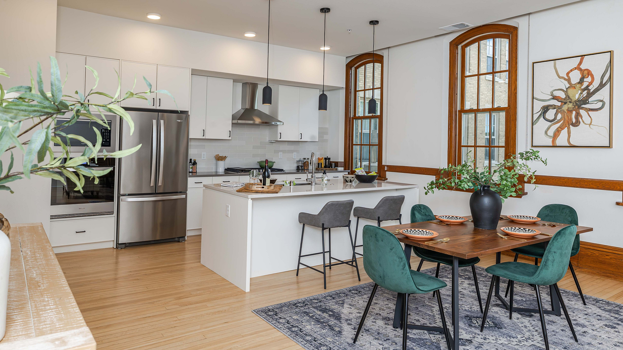 Modern open-concept kitchen and dining area with sleek white cabinetry, stainless steel appliances, chic pendant lighting, and vibrant green dining chairs enhancing spaciousness and elegance.