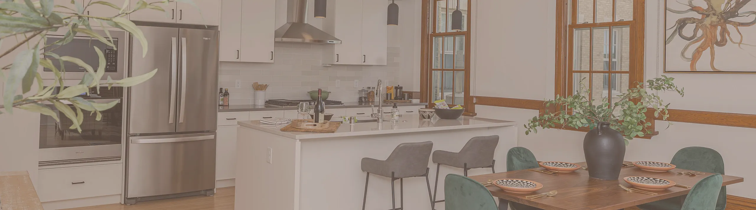 Chic open-concept kitchen and dining area with modern stainless steel appliances, elegant pendant lighting, and stylish green velvet chairs.