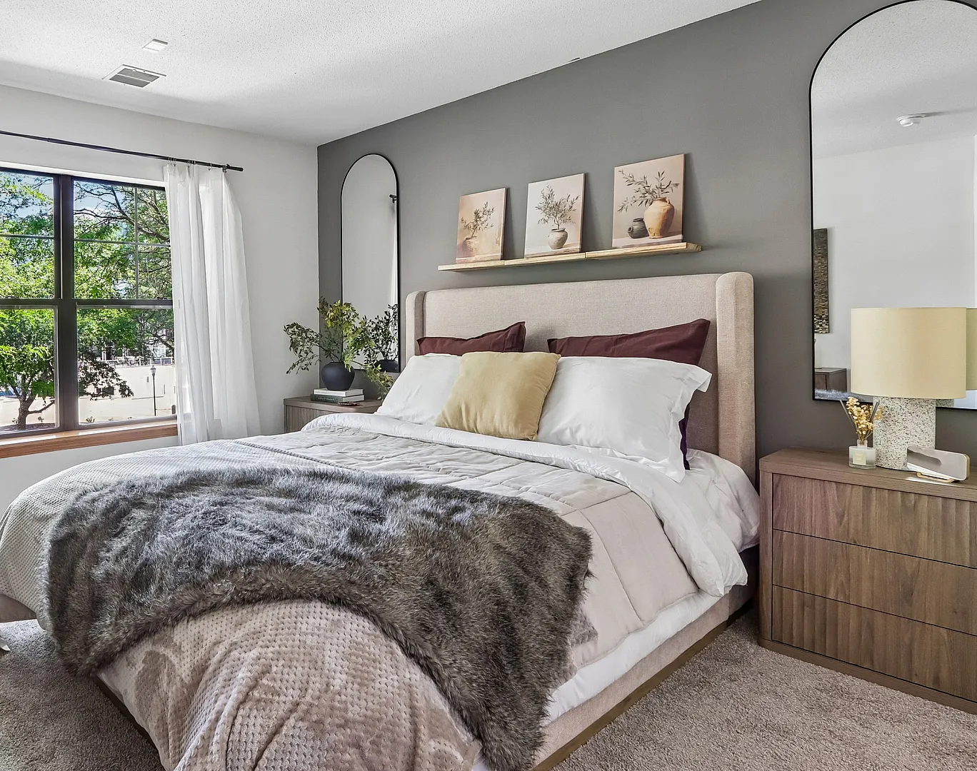 Inviting bedroom with a plush, upholstered bed framed by elegant decor, large window, and stylish wooden furniture, offering a cozy and serene retreat.