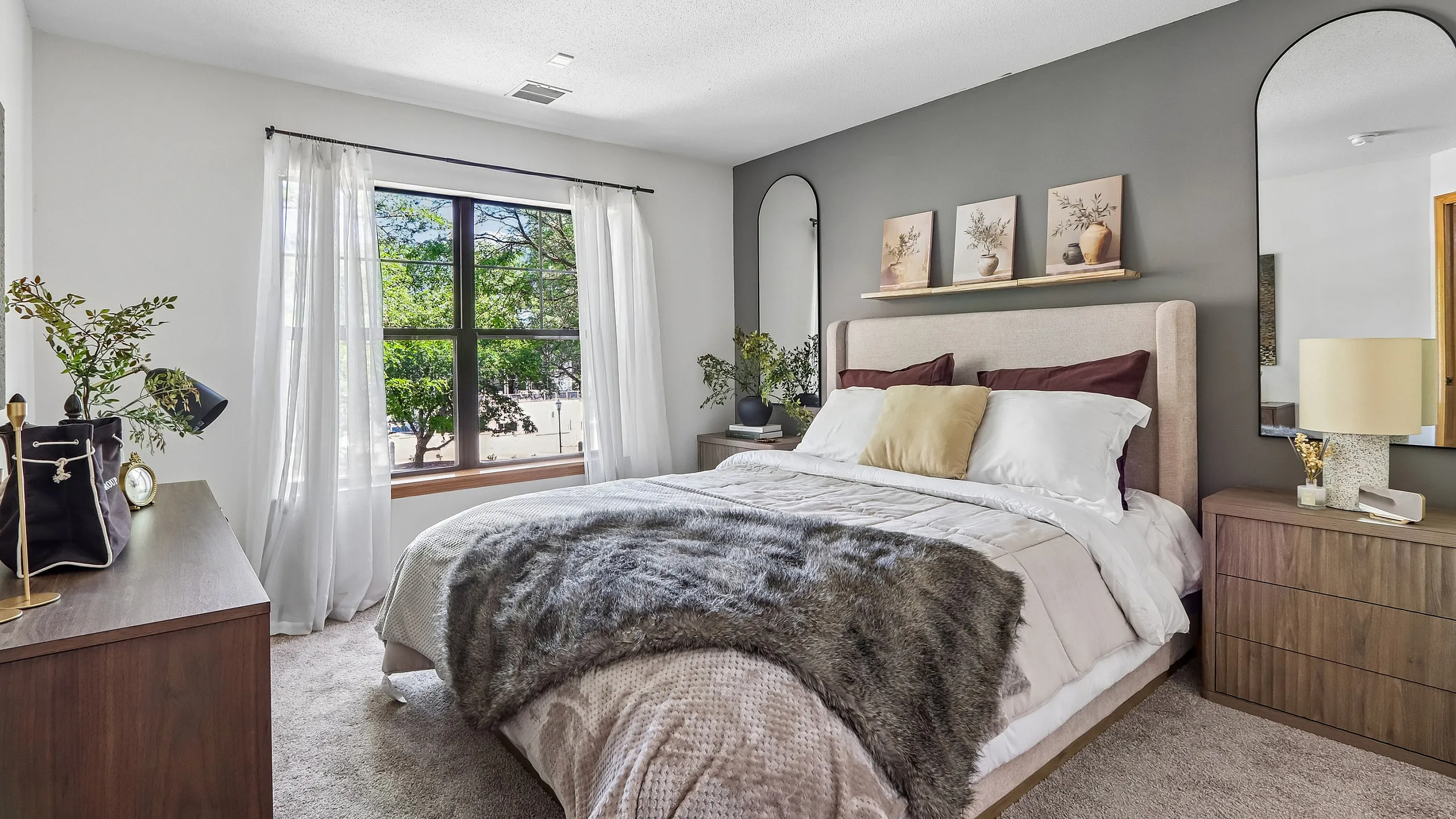 Inviting bedroom with large window, stylish decor, and cozy bed accented by soft textiles and natural light.