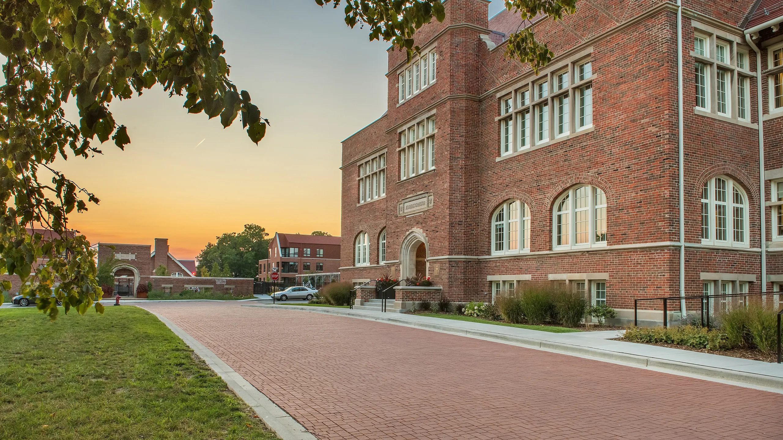 Charming brick building with large arched windows, surrounded by lush greenery, at sunset.