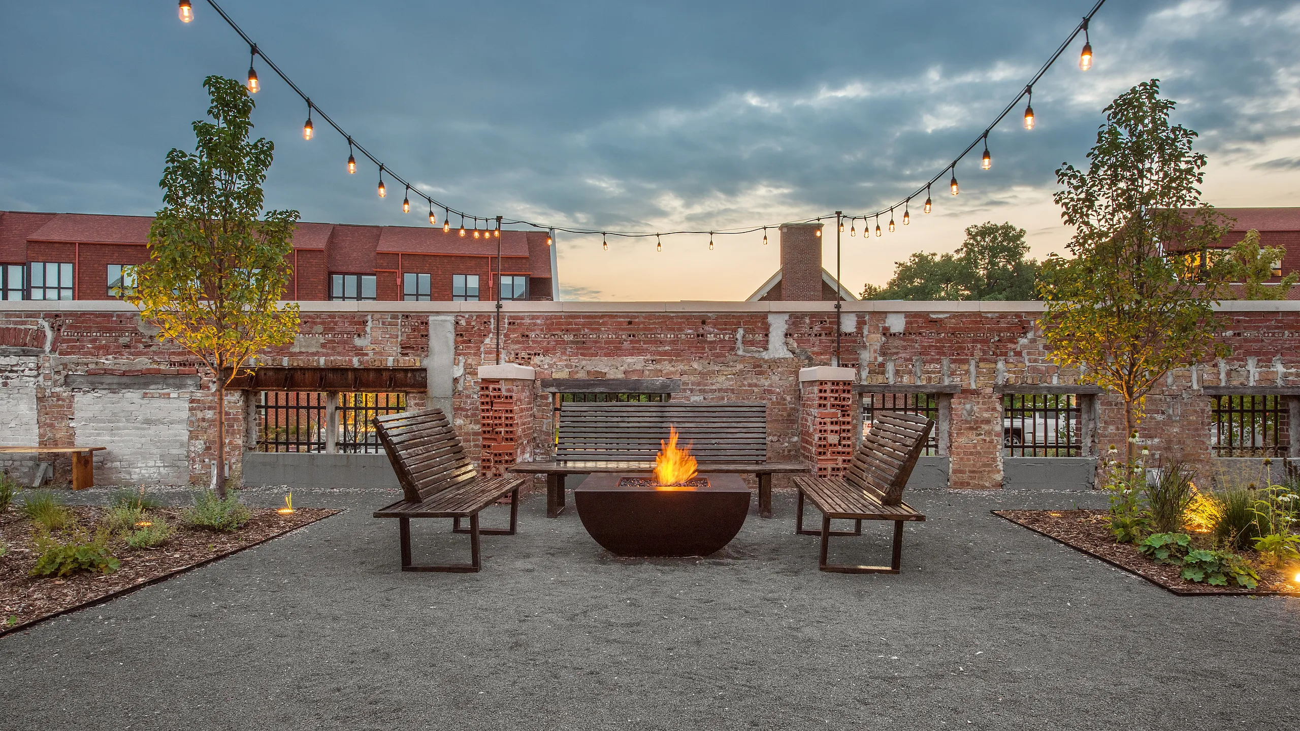 Charming outdoor space with a cozy fire pit, surrounded by wooden benches and illuminated by string lights, offering a perfect setting for evening gatherings.