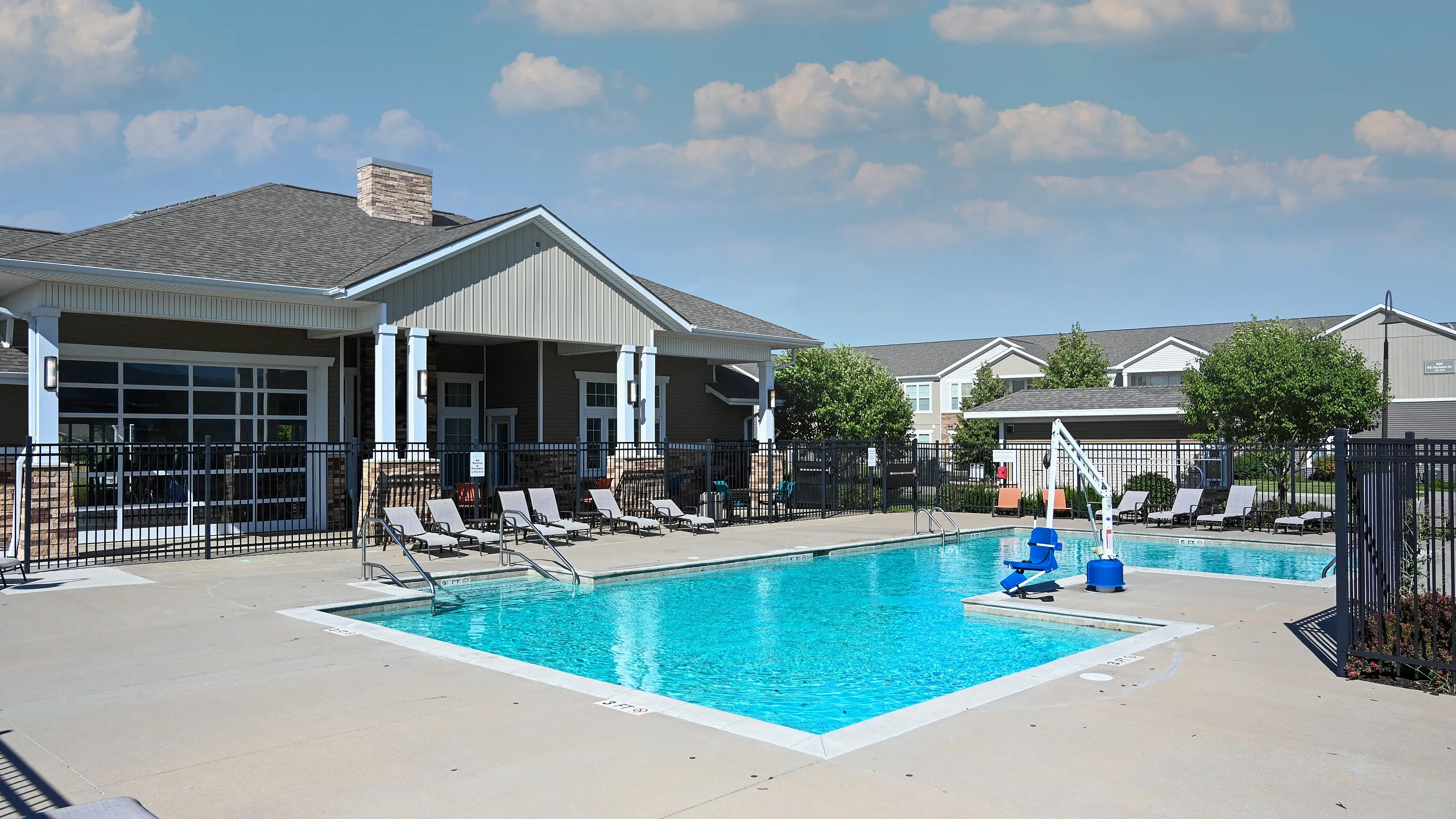 Inviting outdoor swimming pool area with lounge chairs and a modern clubhouse in the background, under a clear blue sky.