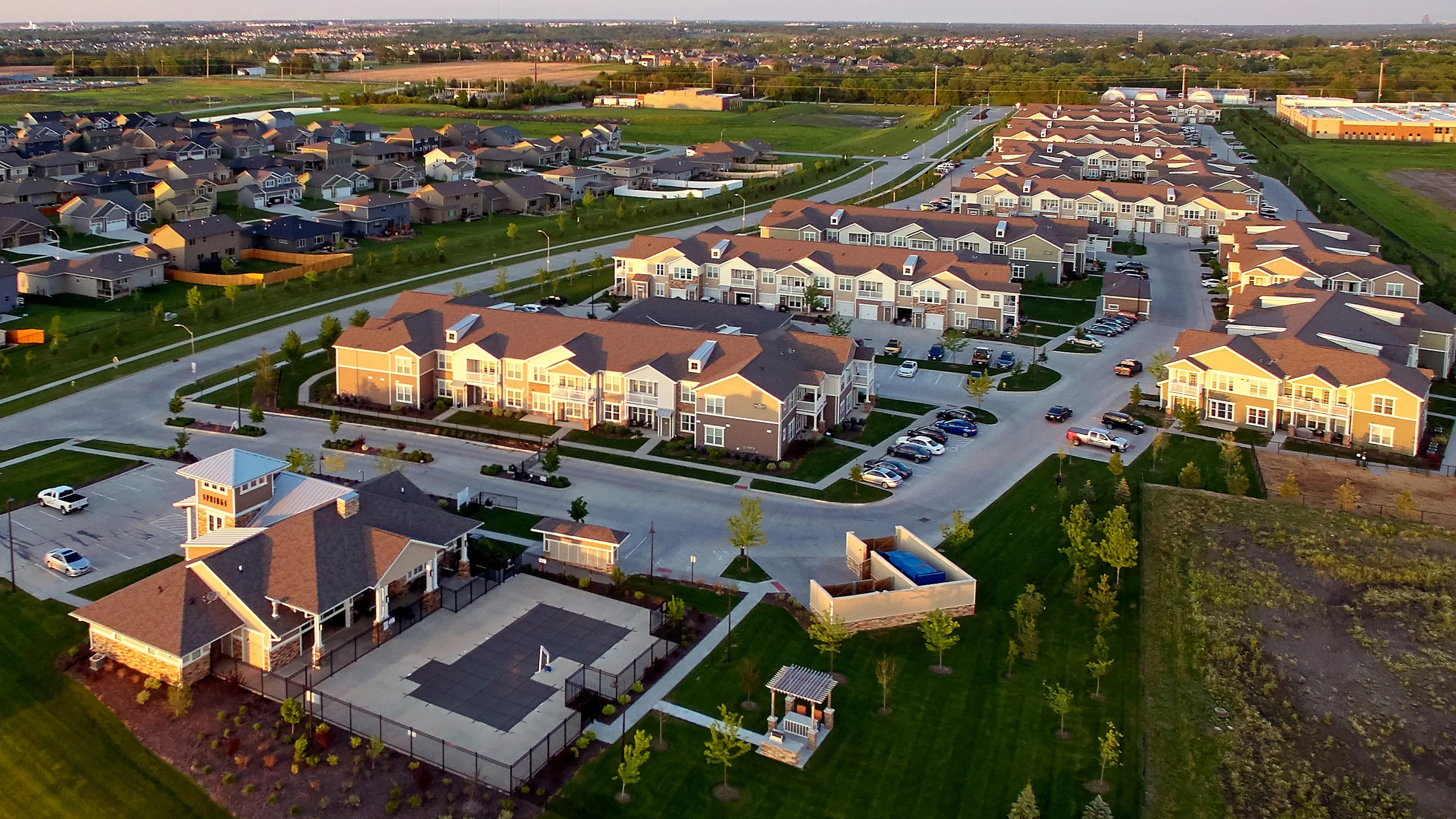 Aerial view of a vibrant residential community with charming townhouses, ample parking, and lush green spaces, featuring a central recreational area with a pool and playground.