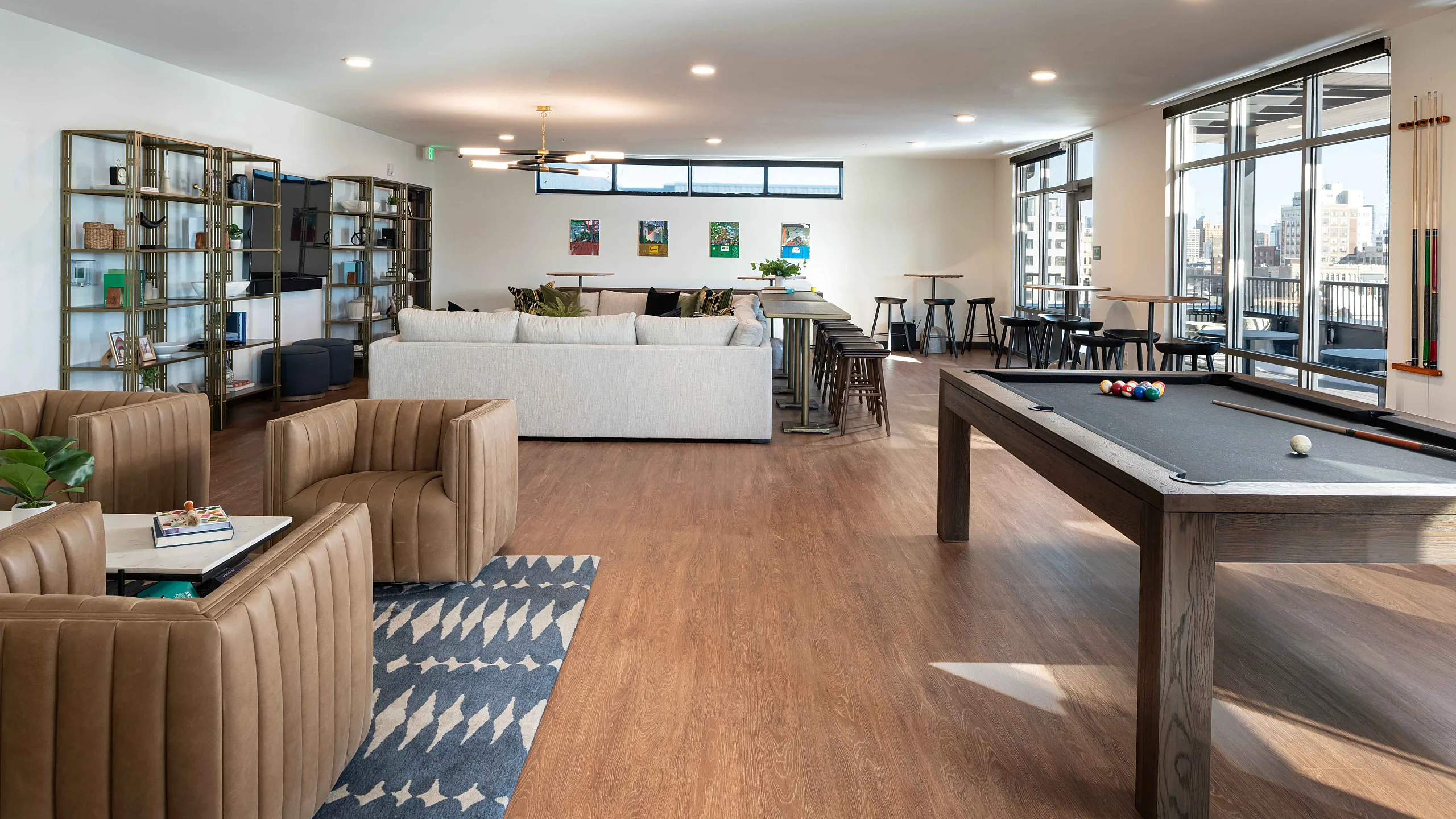 Chic and spacious lounge area featuring modern decor, cozy leather seating, and a stylish pool table with city views.
