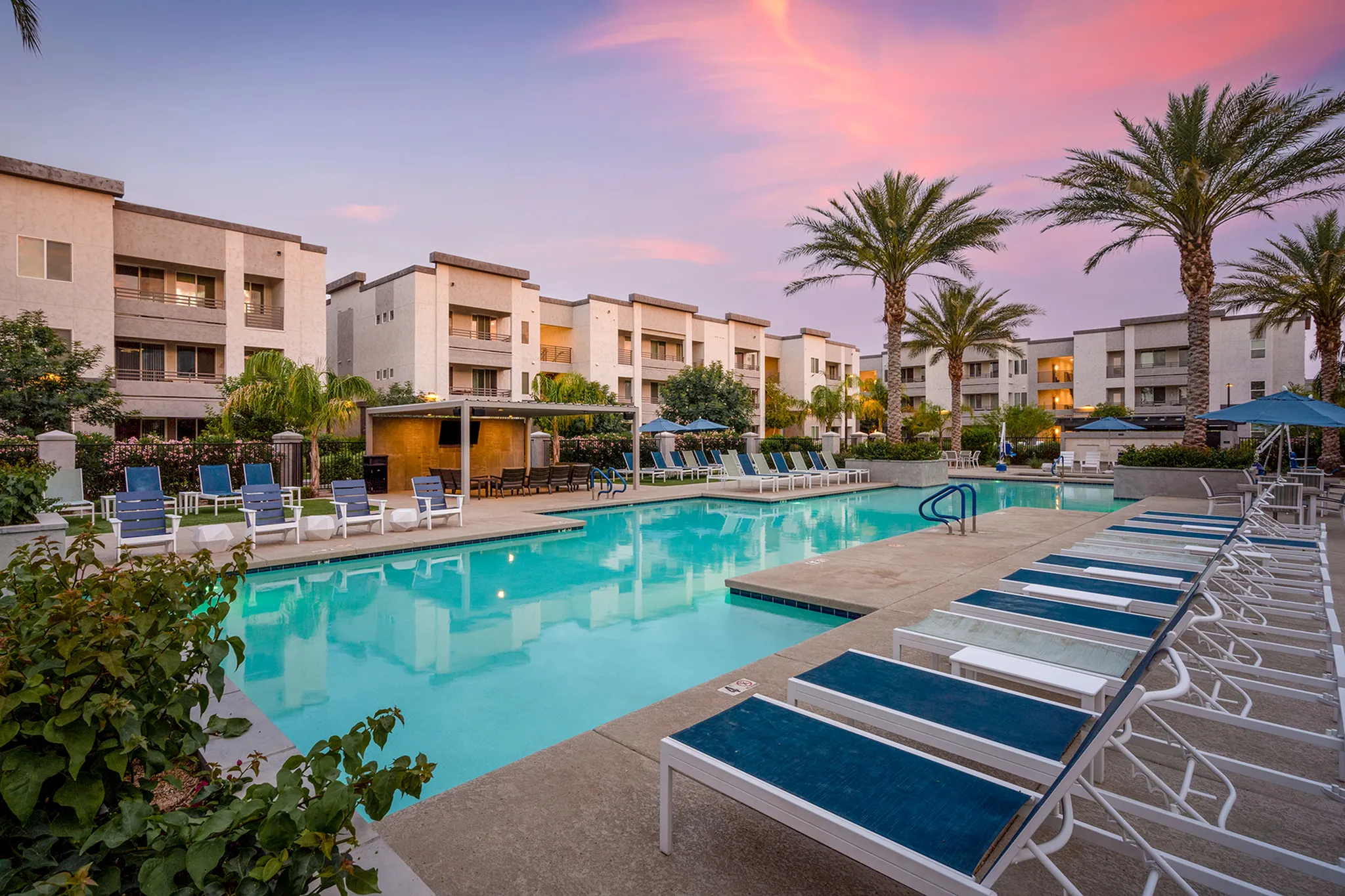 Gorgeous pool area with palm trees, luxury apartments, and sunset sky.