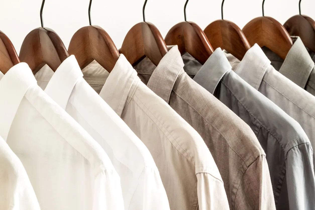 An elegant assortment of dress shirts in varying shades hanging on wooden hangers.