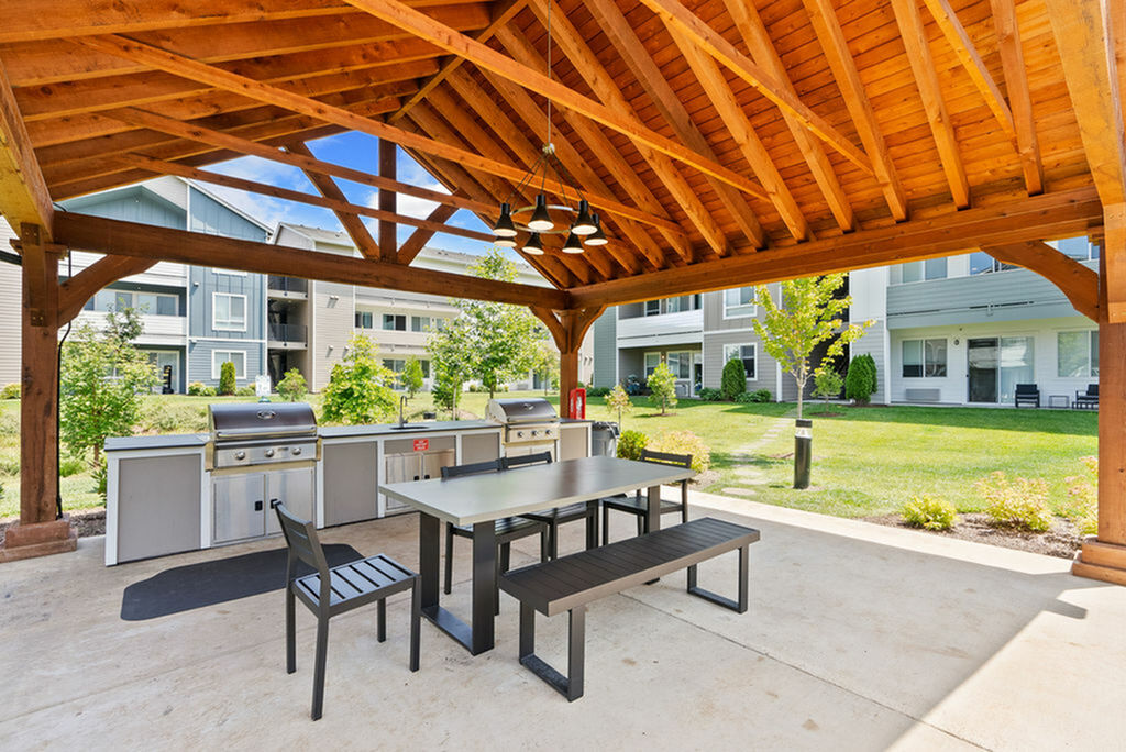 Luxurious outdoor pavilion featuring modern BBQ grills and stylish seating, surrounded by lush greenery in a serene apartment community.