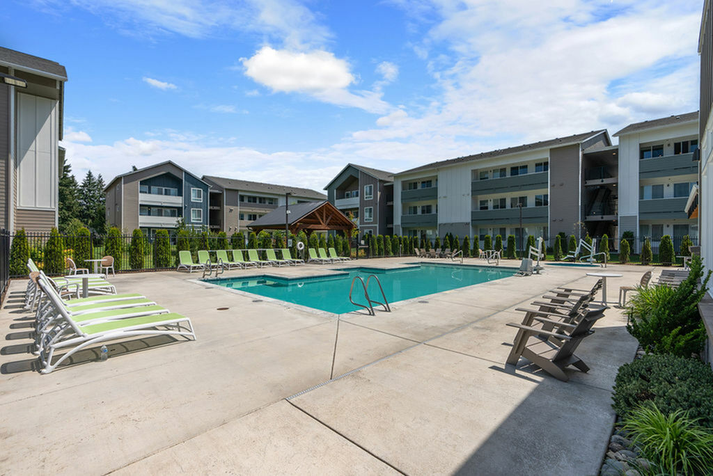 Inviting apartment complex with modern architecture featuring a sparkling outdoor pool and sleek lounge chairs, perfect for relaxation.