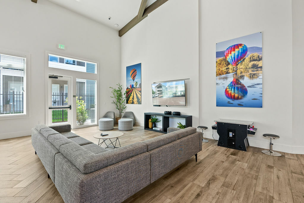 Bright and modern living room with high ceilings, stylish gray sectional, wall art, and natural light streaming through large windows.