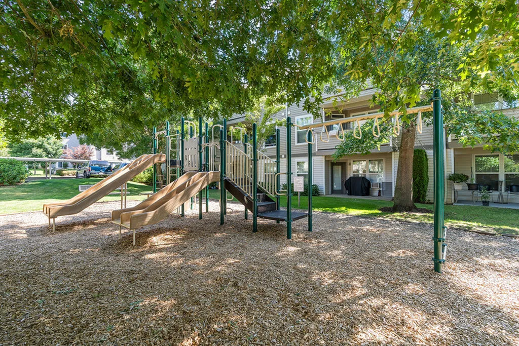 Charming playground nestled under lush trees with modern slides, ideal for families in a serene apartment complex.