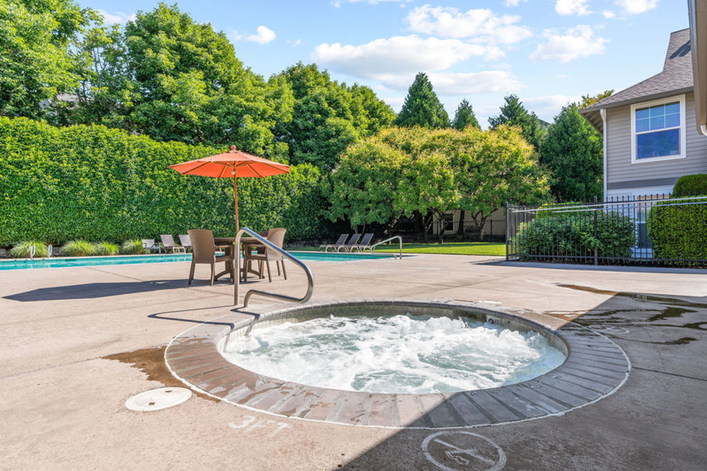Inviting outdoor area featuring a bubbling hot tub, shaded seating with umbrellas, and lush greenery, perfect for relaxation and leisure.