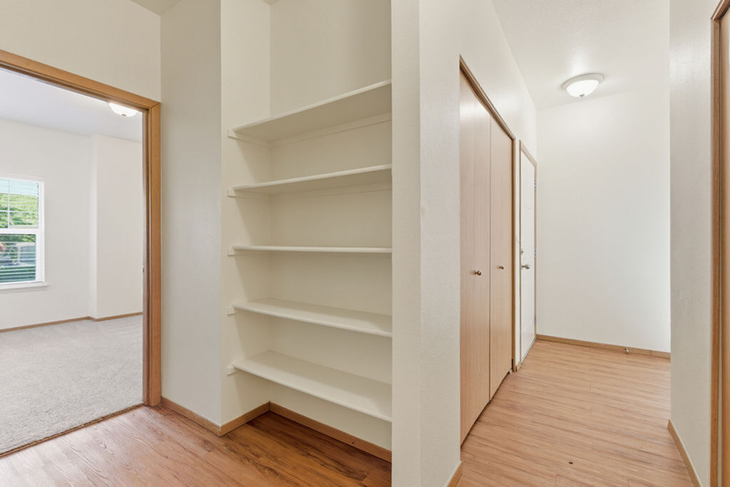 Bright, airy apartment with a hallway featuring built-in shelves, elegant wooden flooring, and access to a sunlit bedroom.
