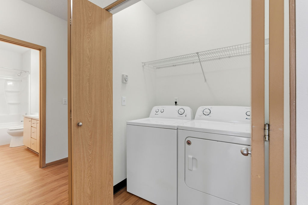 Modern apartment with in-unit laundry and adjacent bathroom featuring sleek wood flooring and ample cabinetry.