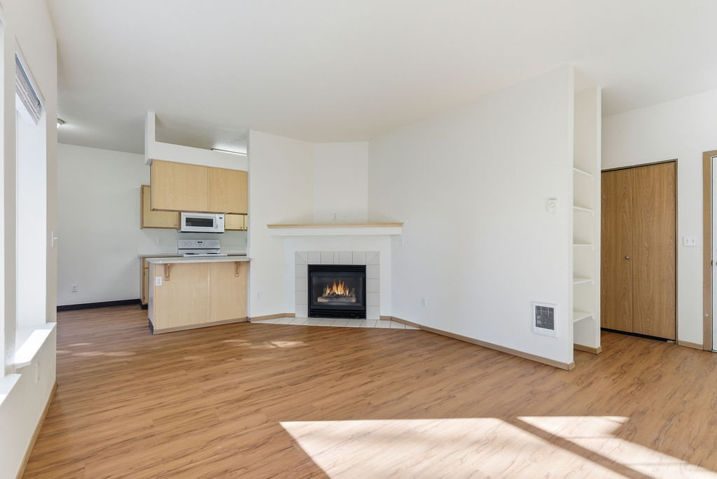 Bright open-plan living area featuring a cozy fireplace and modern kitchen with ample natural light and stylish flooring.