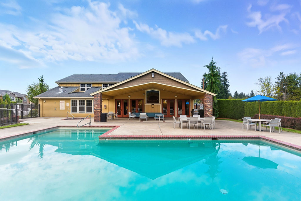 Inviting apartment complex featuring a crystal-clear swimming pool with elegant poolside seating and a charming clubhouse under a serene blue sky.