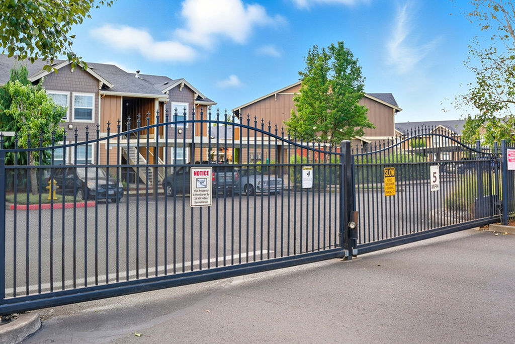 Secure and inviting community entrance with elegant wrought iron gates and charming, modern townhouses in a lush setting.