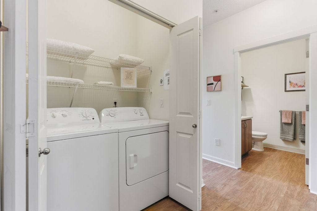 Chic apartment laundry area with modern washer and dryer adjacent to a stylish bathroom, featuring sleek wooden floors and elegant shelving.
