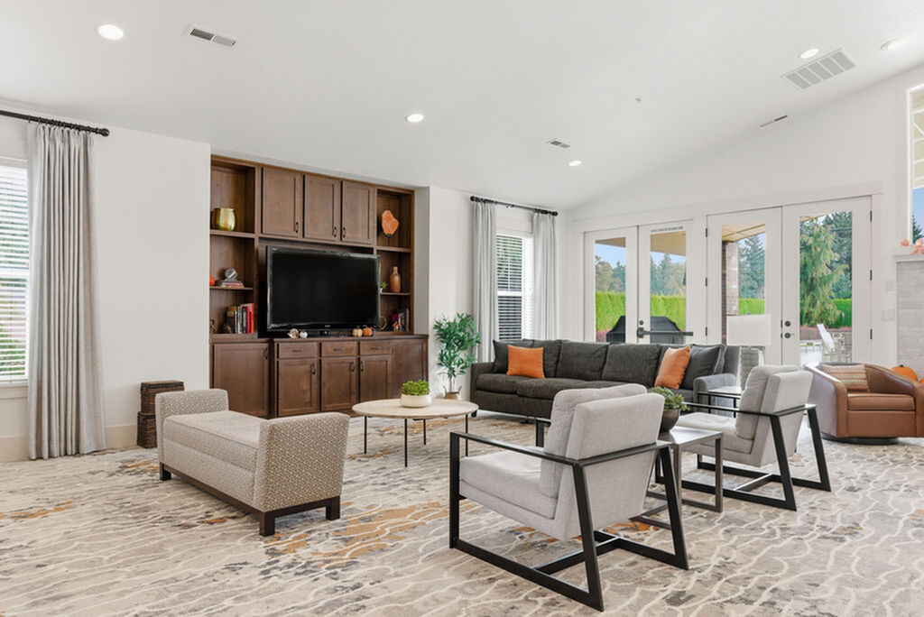 Modern and inviting living room with elegant furniture, cozy armchairs, and a large wooden entertainment center, complemented by abundant natural light through expansive glass doors.