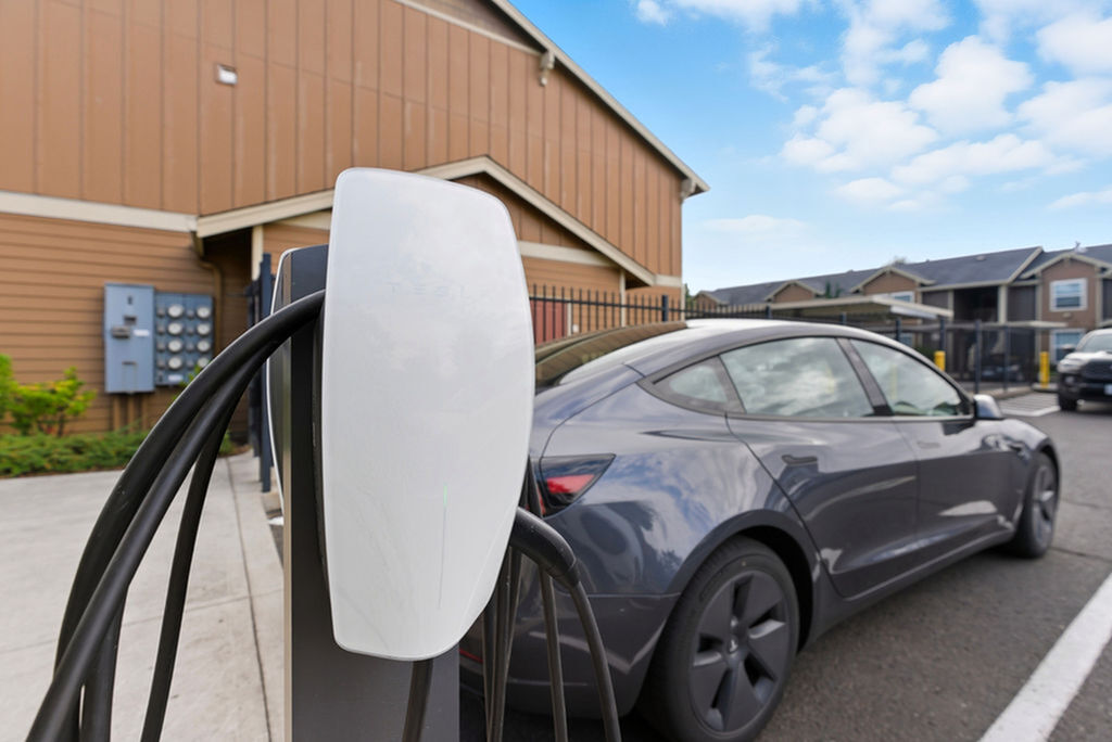 Contemporary apartment complex with EV charging station and sleek electric vehicle, emphasizing sustainable living.