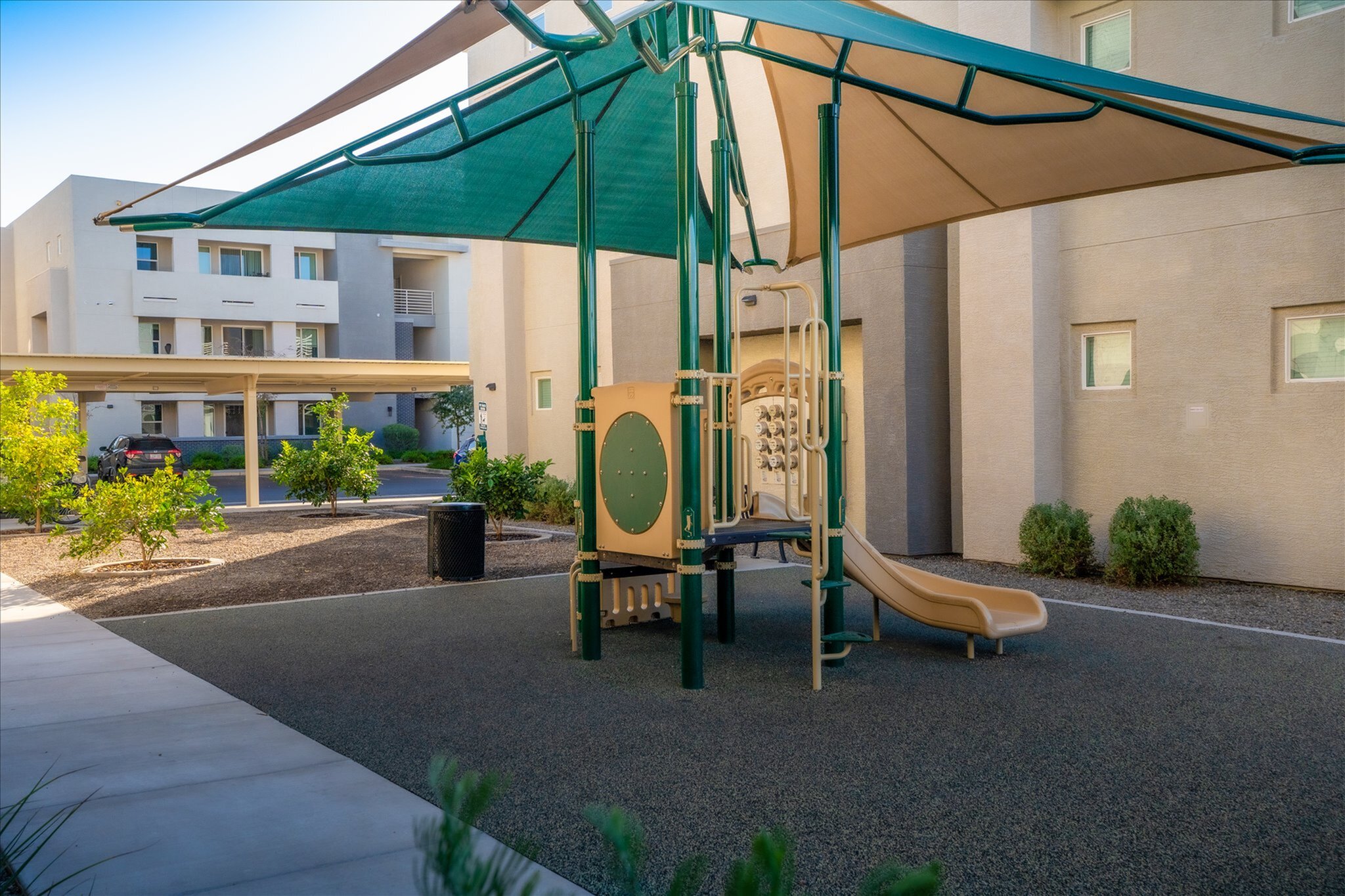 Inviting playground area with modern equipment and shade structures, set amidst a vibrant apartment complex.