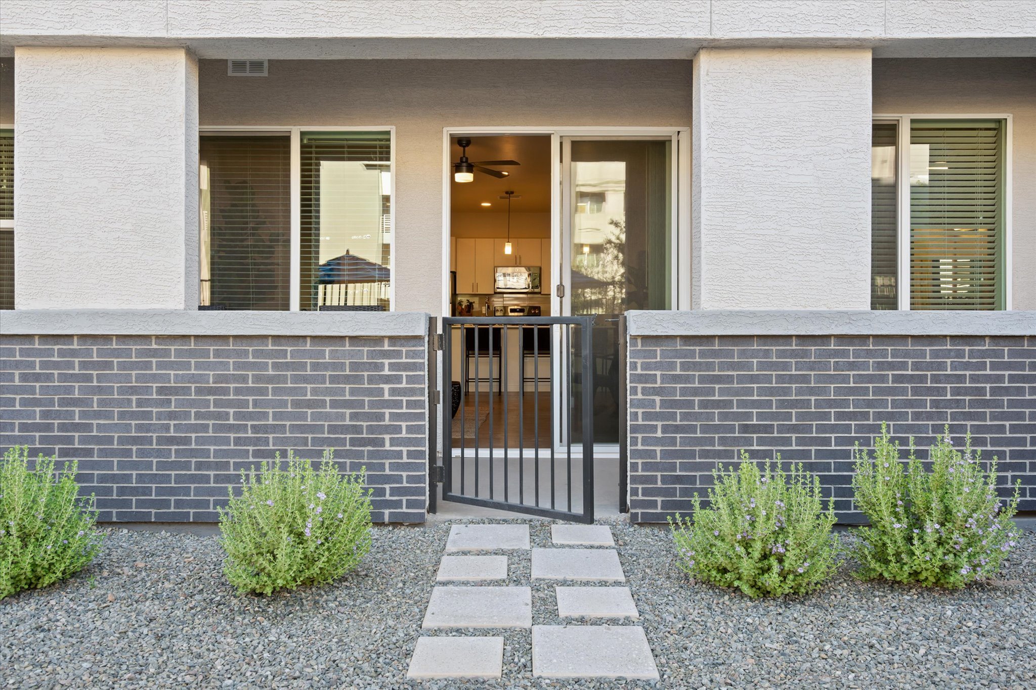 Charming apartment entrance with modern brick facade, lush landscaping, and inviting open door leading to a cozy interior.