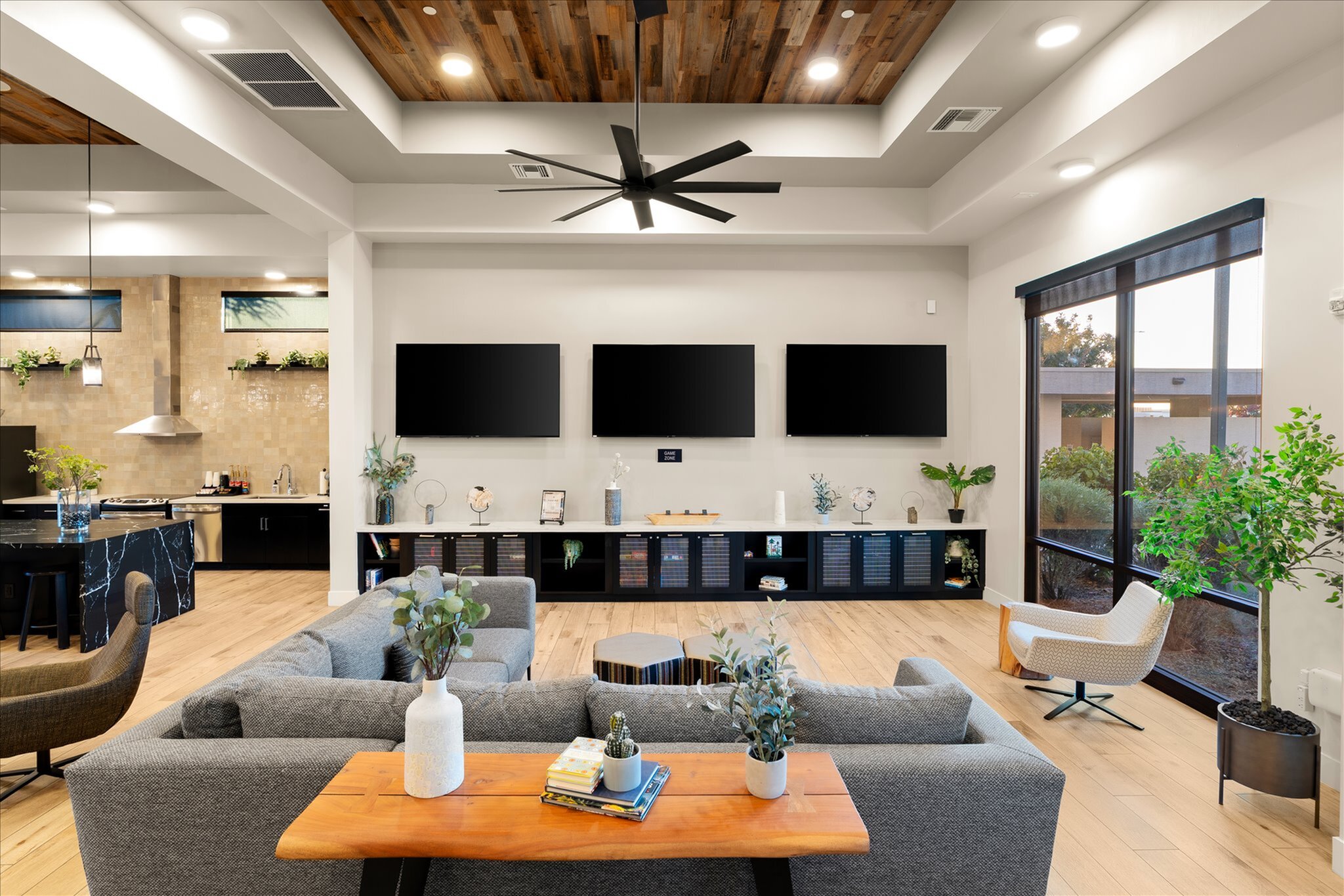 Modern community room featuring a stylish open-concept design with sleek wood accents, multiple flat-screen TVs, and abundant natural light.