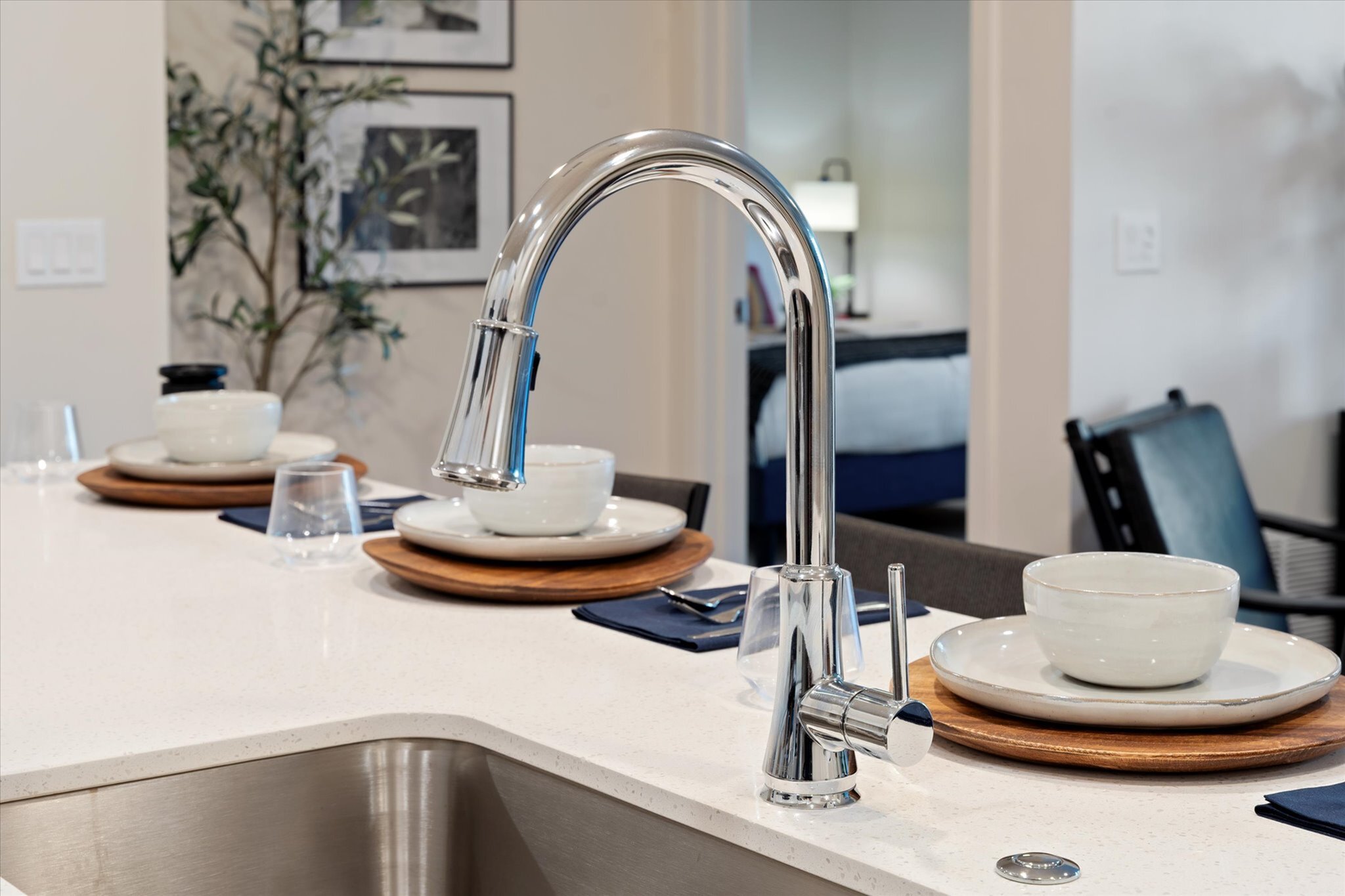 Modern kitchen space showcasing a sleek chrome faucet, elegant dining setup with minimalist tableware, and a glimpse of the cozy adjoining room.
