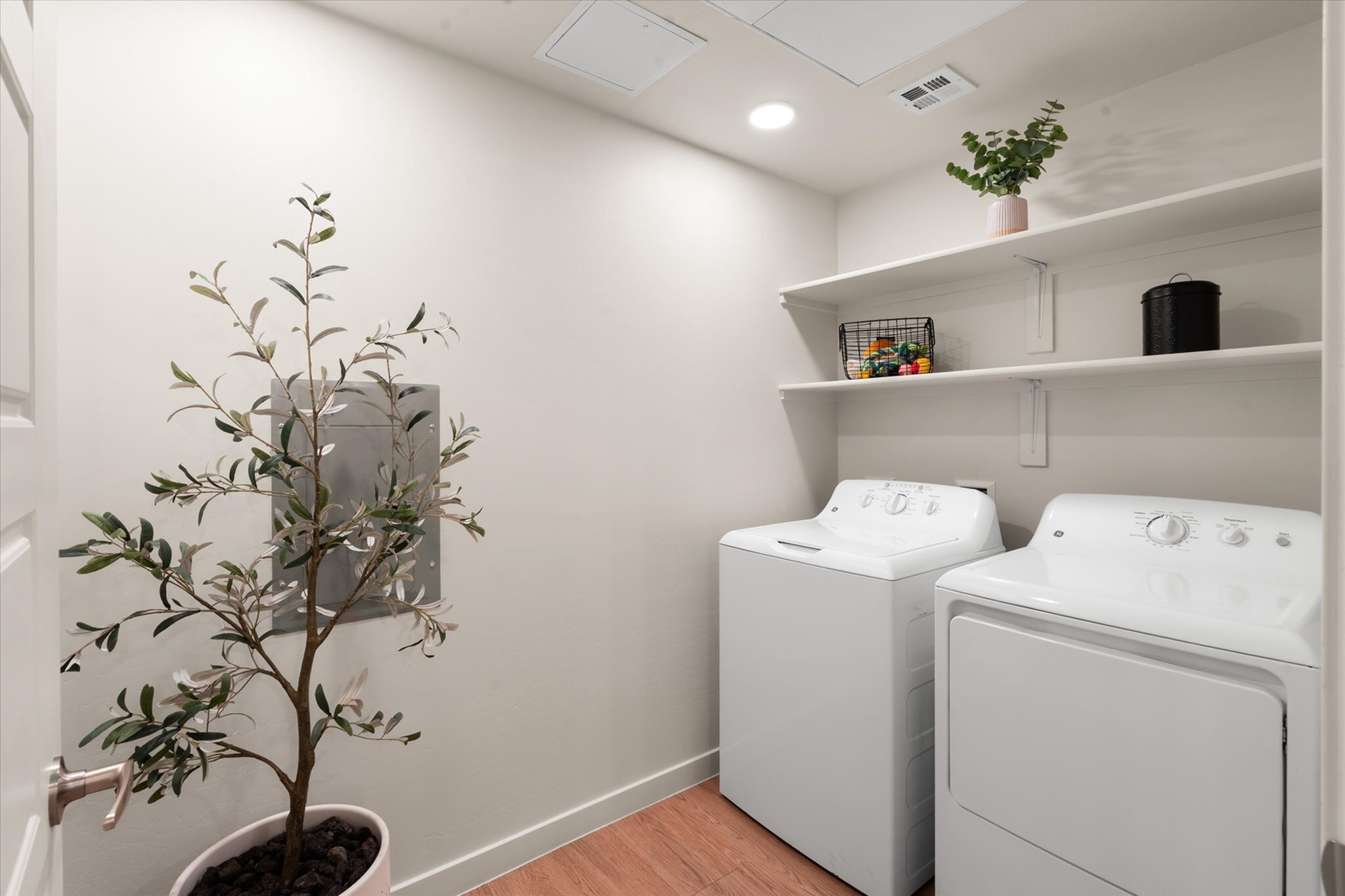 Bright laundry room with modern washer and dryer, elegant shelving for storage, and a decorative potted plant adding charm.