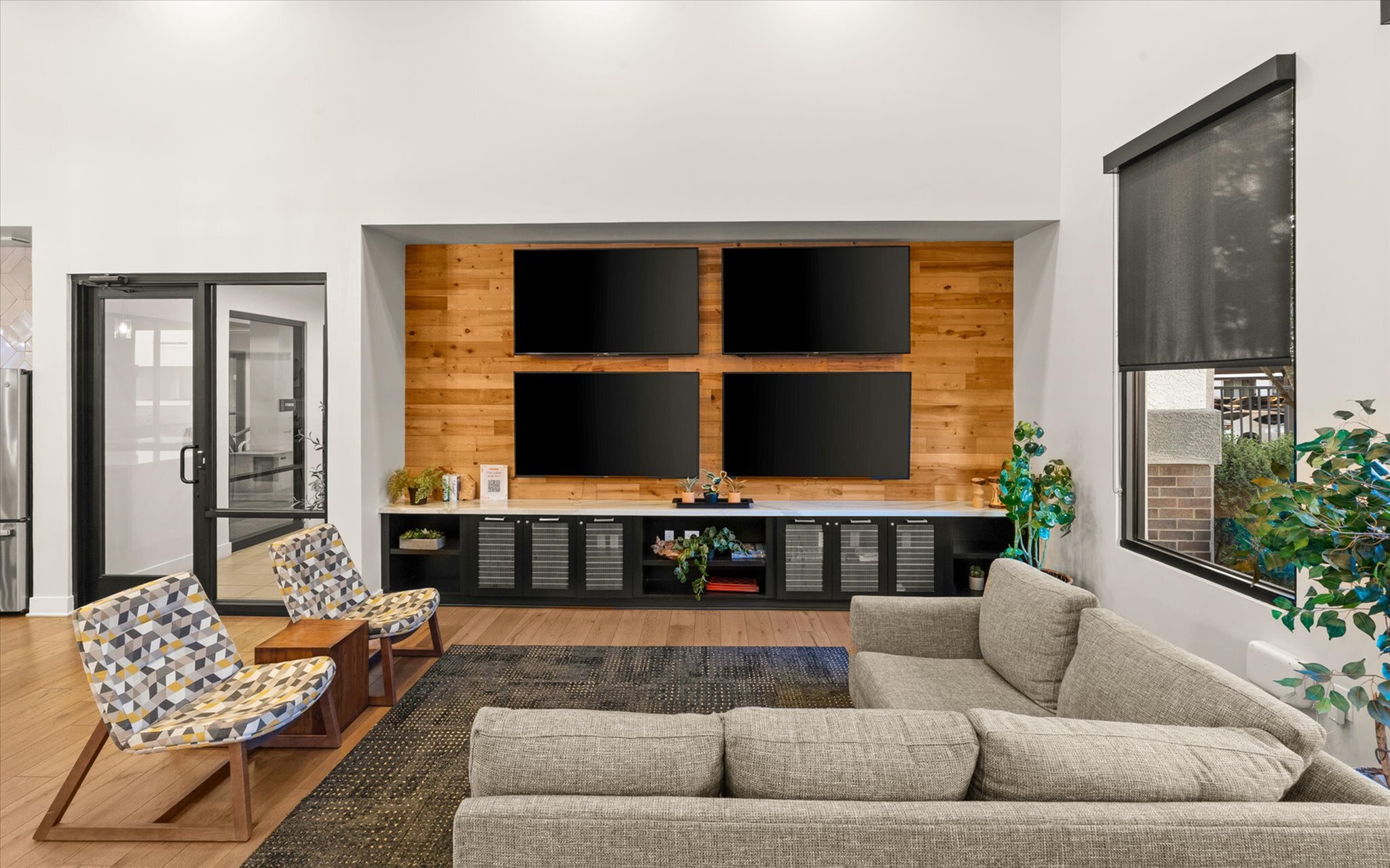 Modern living room with four large TVs on a wooden feature wall, stylish seating, and abundant natural light.