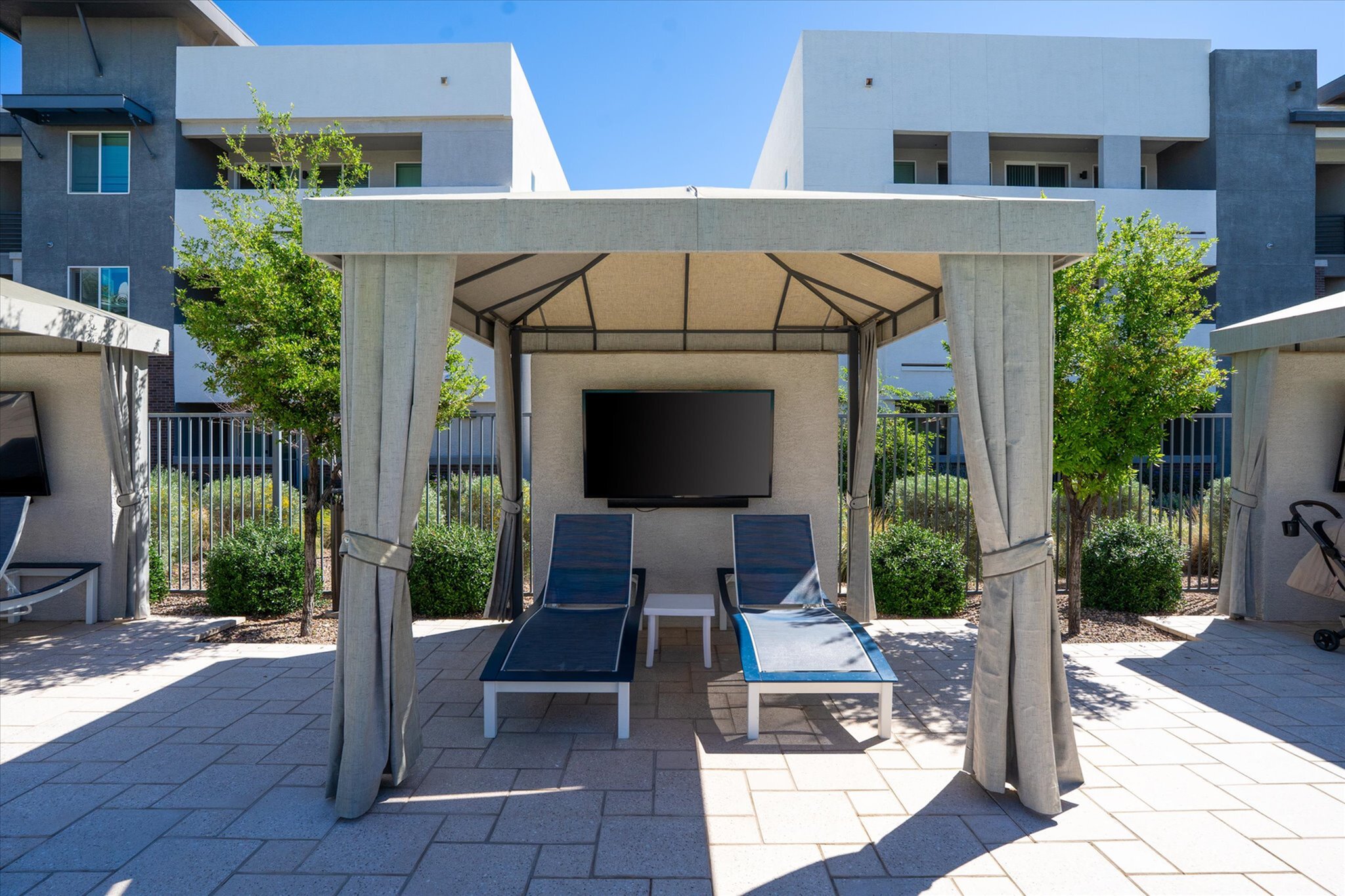 Luxurious outdoor cabana featuring two stylish lounge chairs and a wall-mounted TV, perfect for relaxation and entertainment.