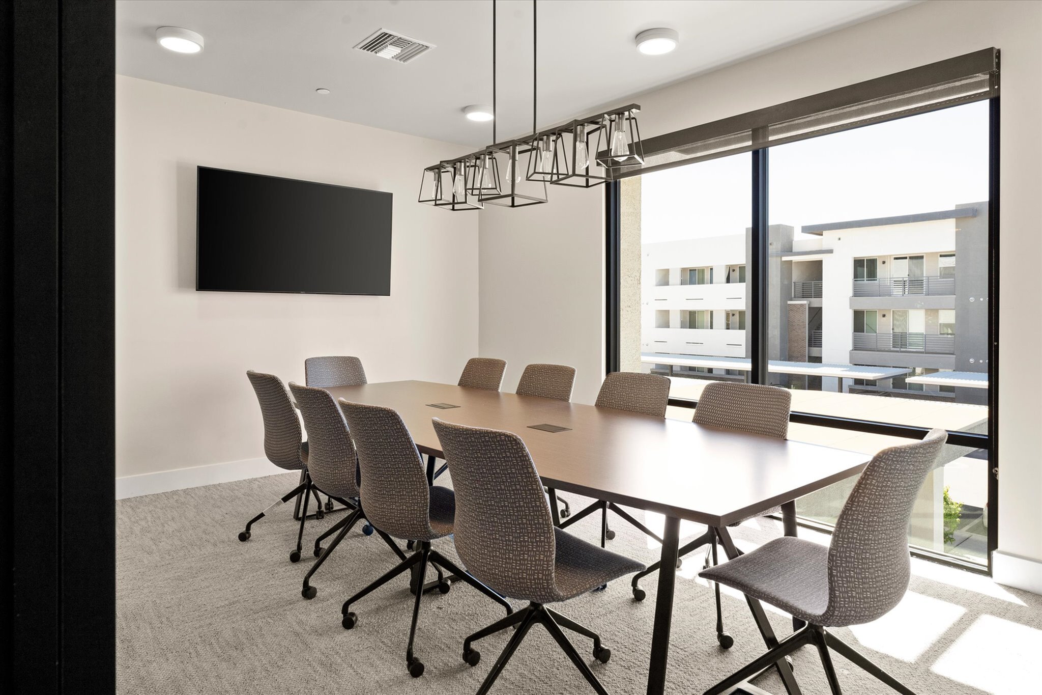 Modern conference room with sleek furnishings, a large window offering abundant natural light, and contemporary lighting fixtures.