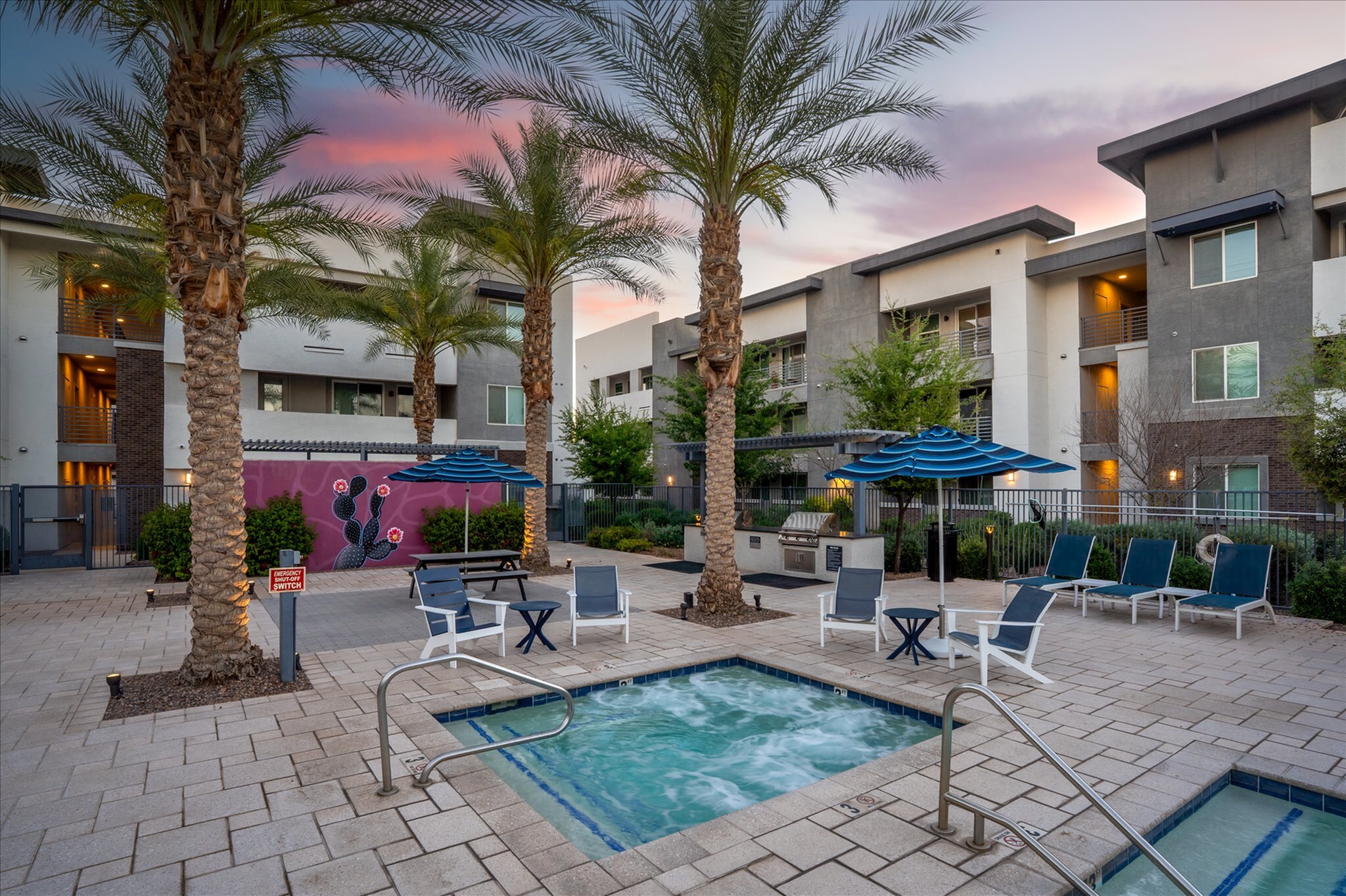 Luxurious apartment complex featuring a serene outdoor area with palm trees, a heated jacuzzi, and stylish lounge seating, perfect for relaxation and entertaining.