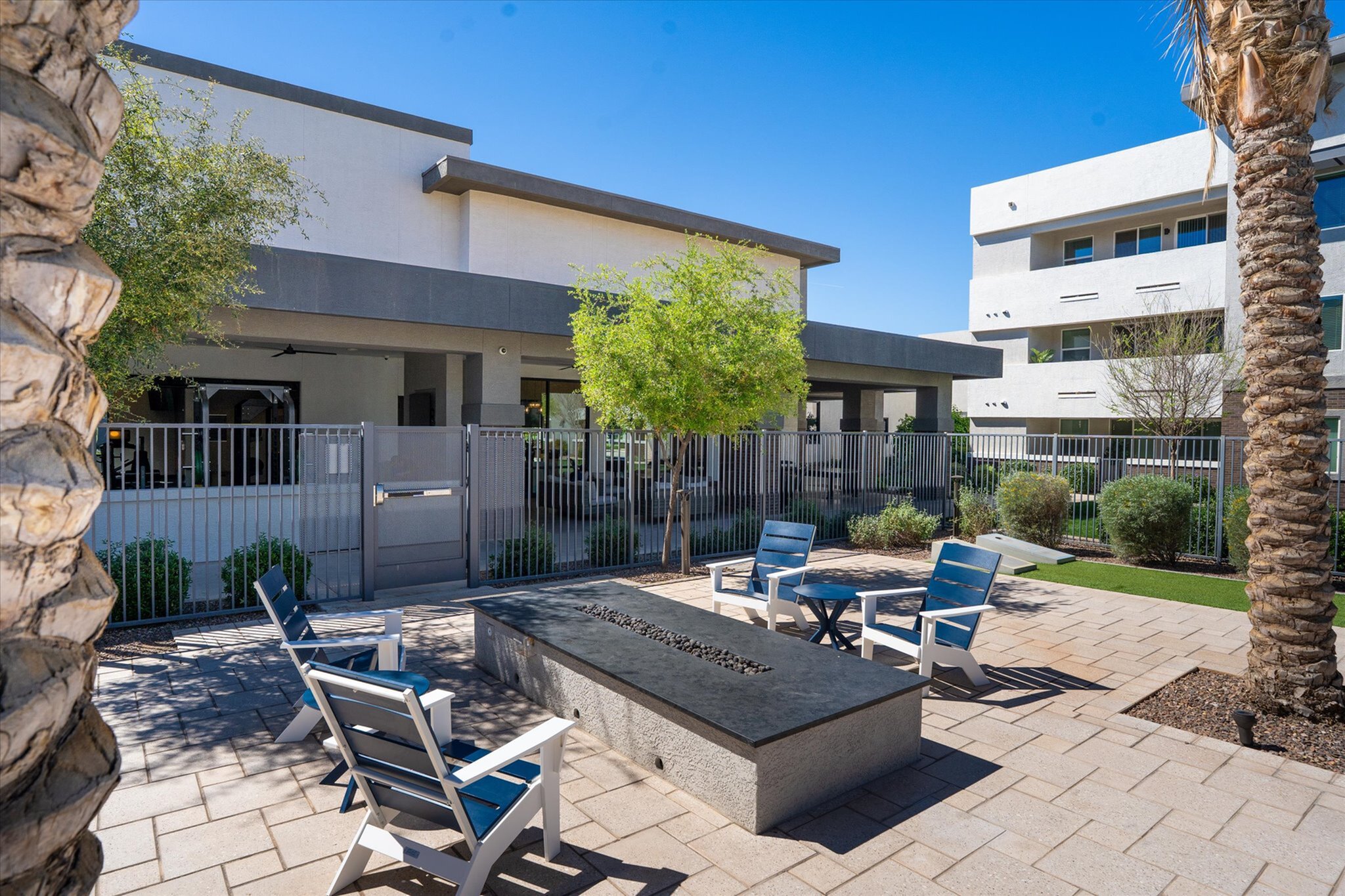 Modern outdoor seating area with stylish chairs and a sleek fire pit, surrounded by lush greenery and contemporary architecture.