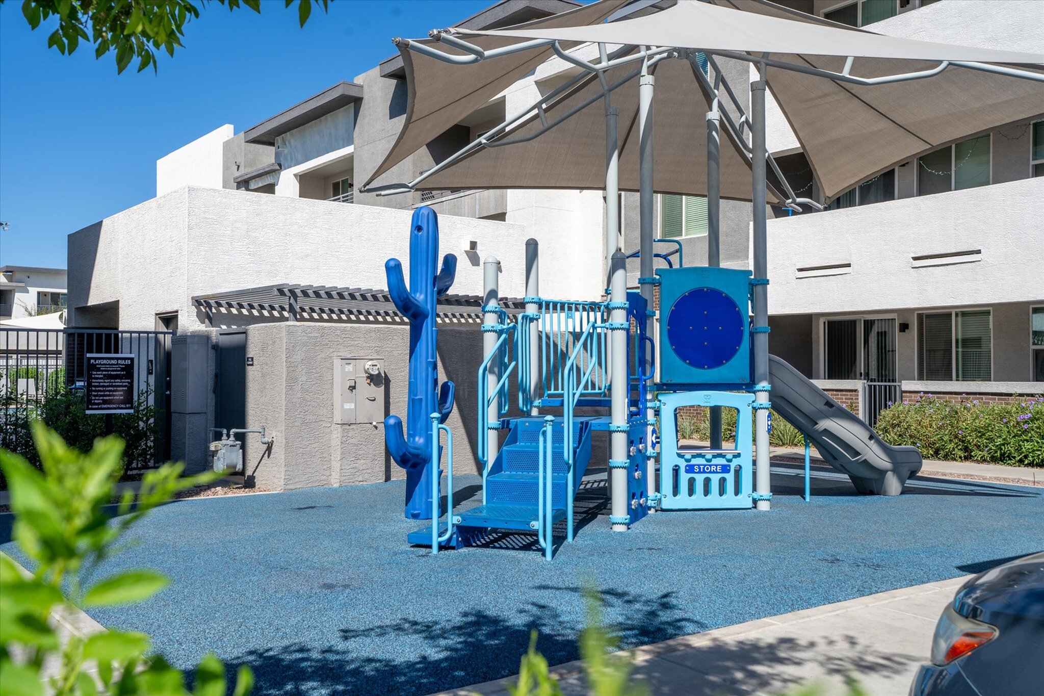 Modern apartment complex playground featuring vibrant blue play structures under a stylish canopy.