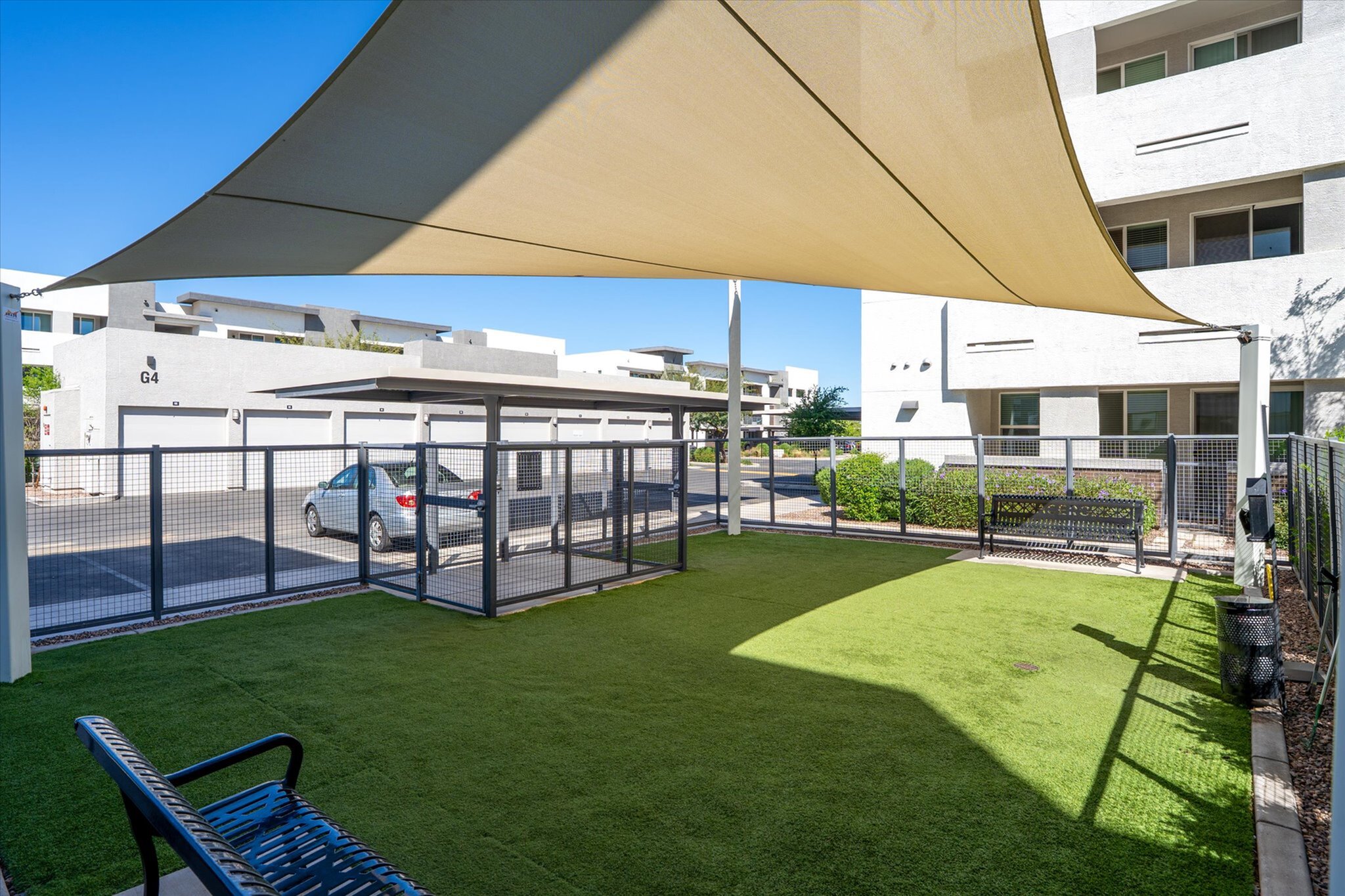 Dog park with sunshade, lush green lawn, and modern seating.