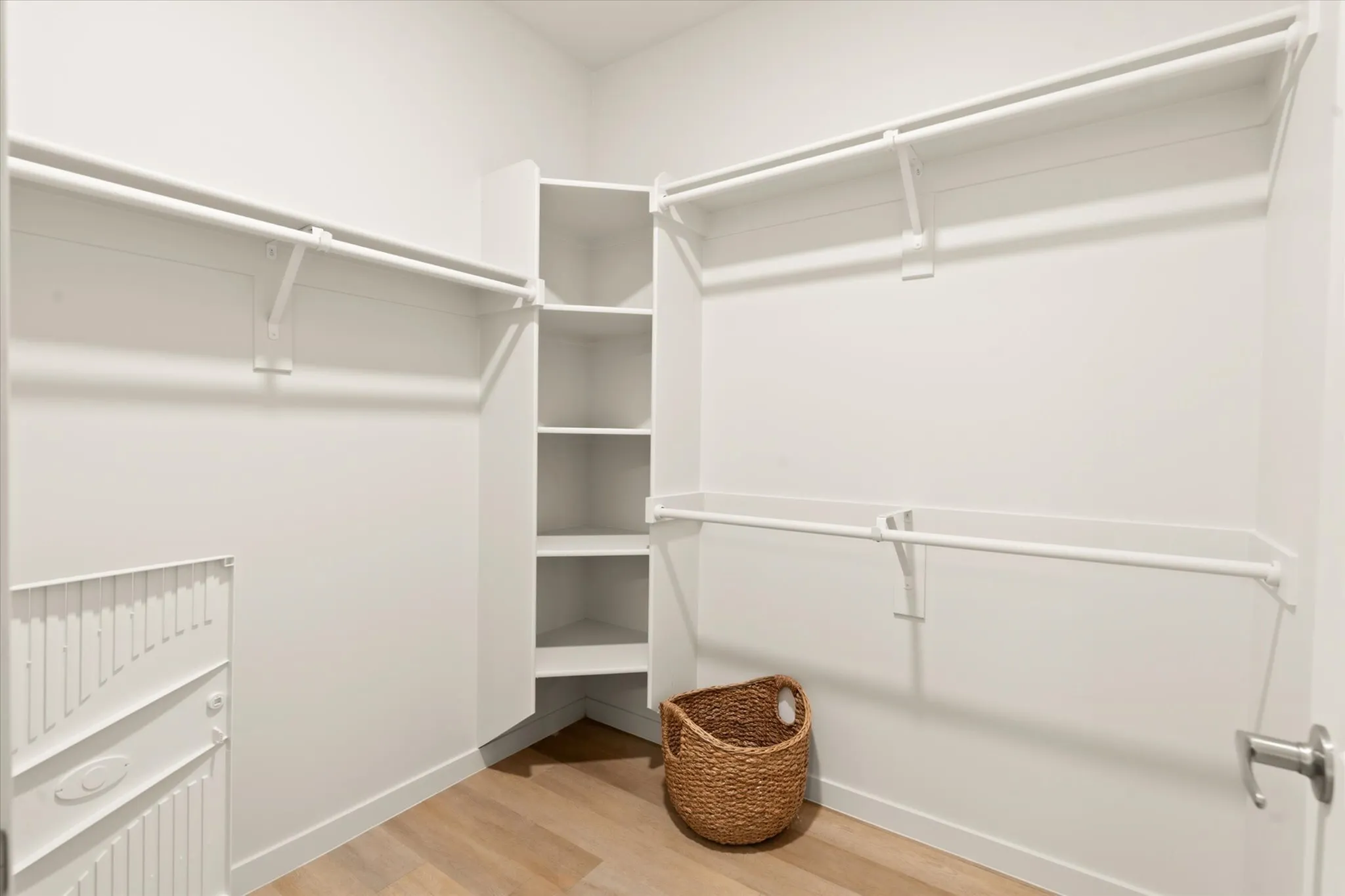 Elegant walk-in closet with ample shelving and hanging space, featuring a chic woven basket on stylish wood flooring.